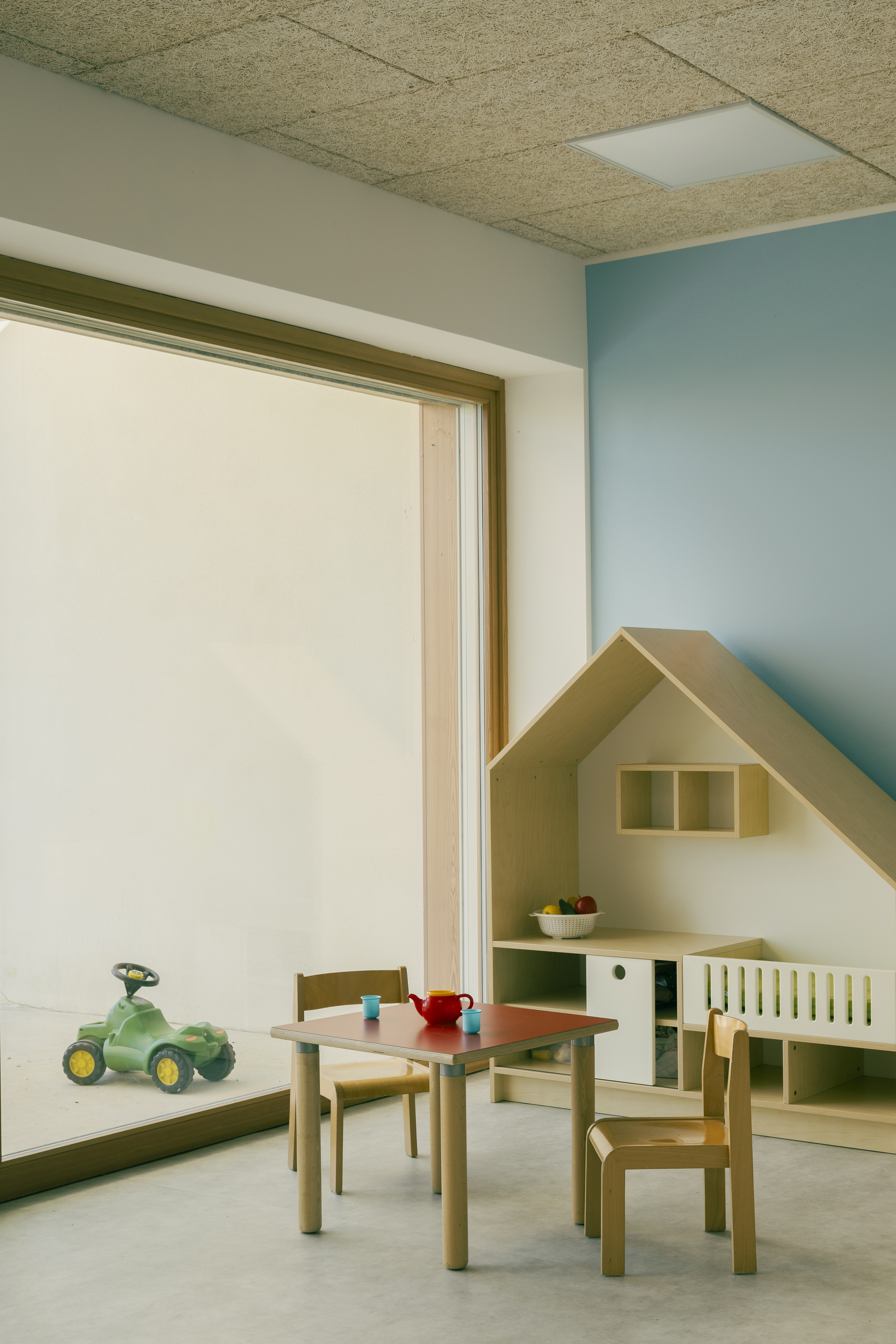 Interior playroom with house-shaped storage unit against a blue wall beneath a cork panel ceiling