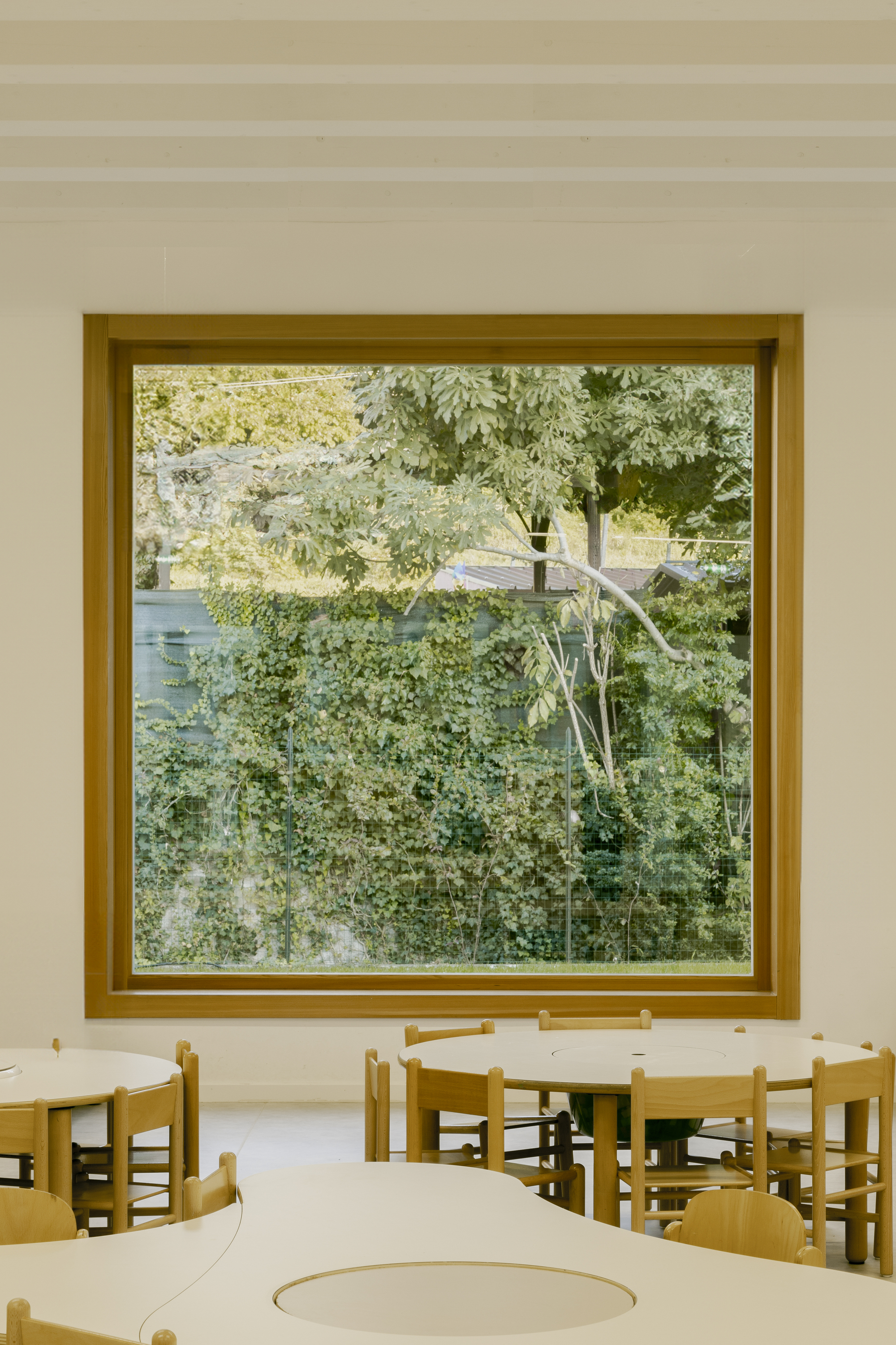 Large timber-framed window overlooking dense green foliage with children's tables and chairs in the foreground