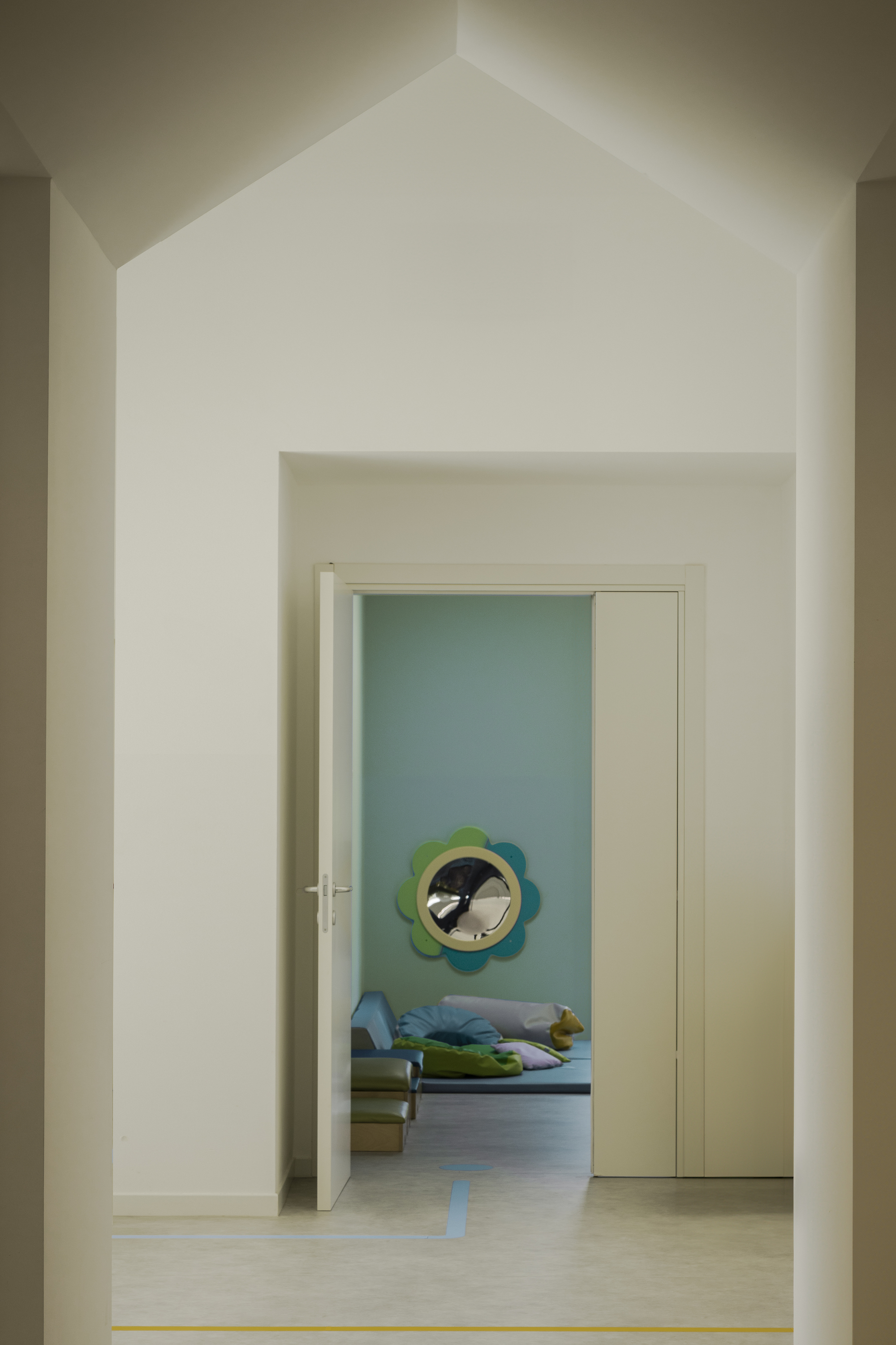 View through a doorway with gabled ceiling into a sleeping room with a circular wall mirror