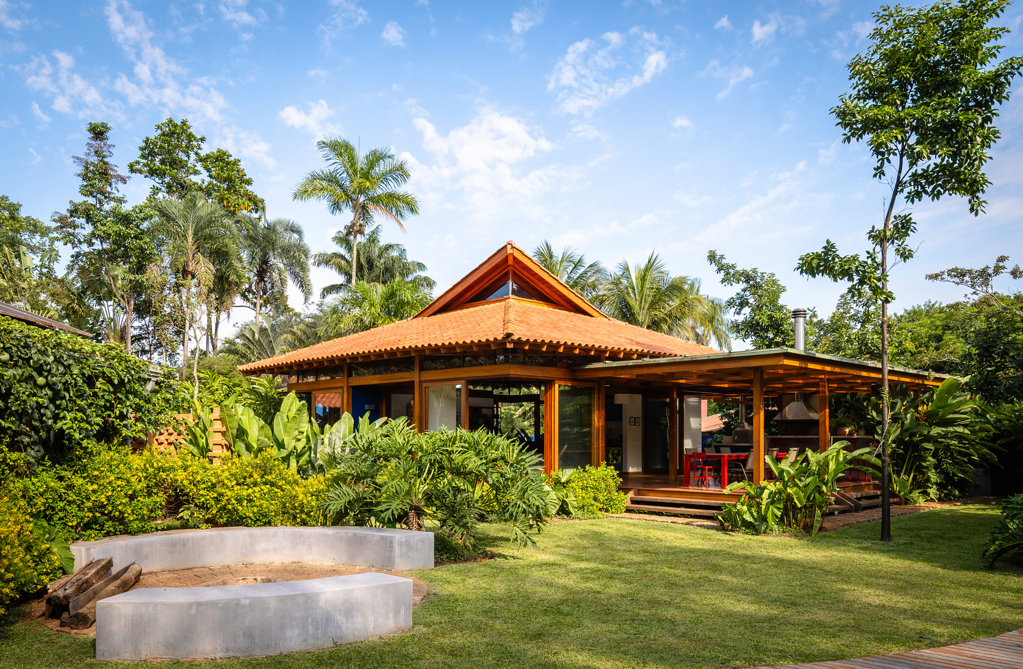 Garden view of open-sided pavilion with terracotta tile roof and concrete bench under palm trees