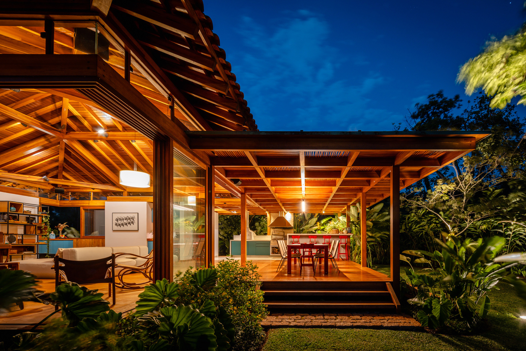 Covered terrace with exposed timber beam ceiling and glazed walls opening to dining area at night