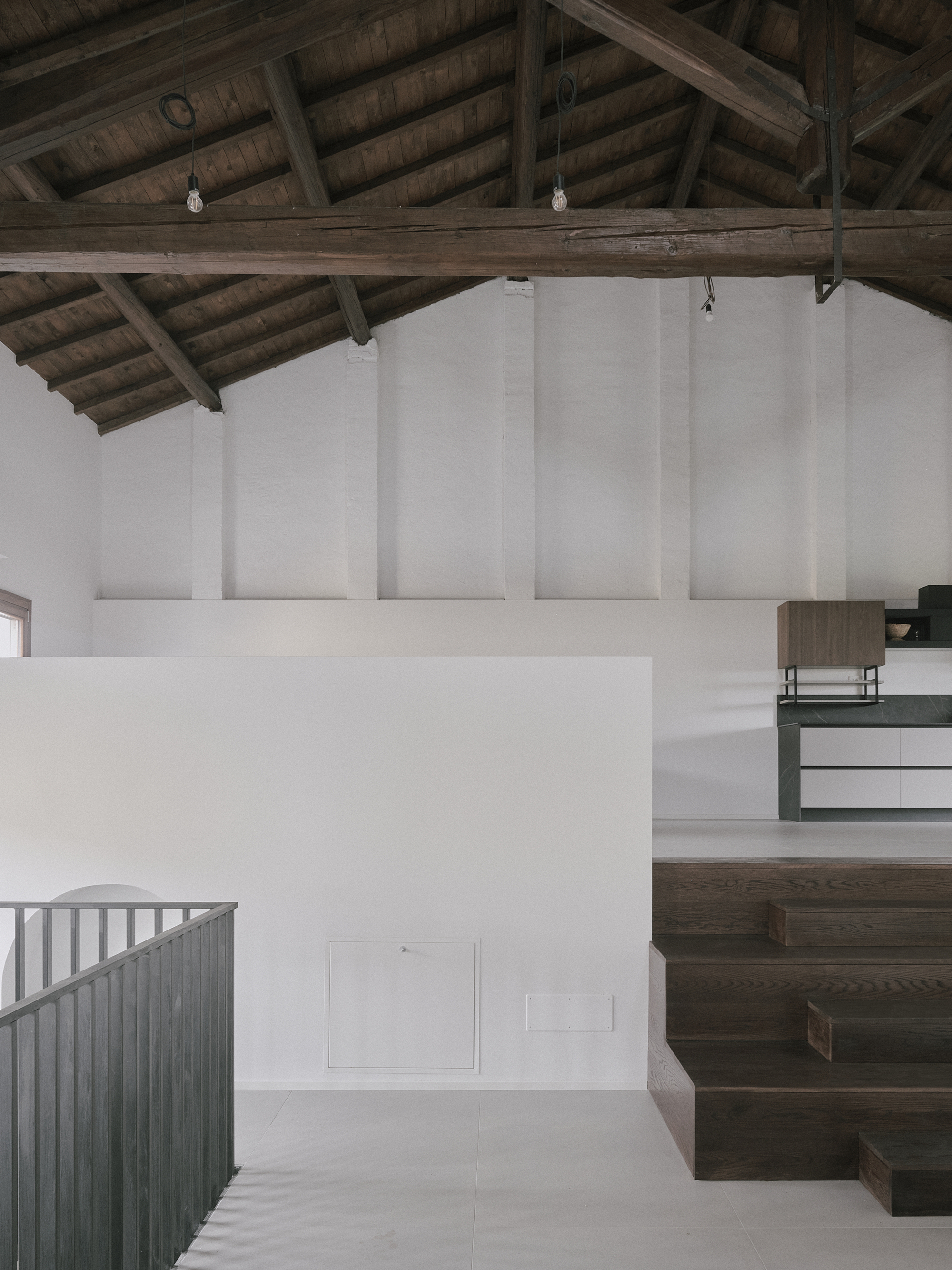 Interior view of dark timber staircase rising beneath exposed wooden roof trusses and white walls