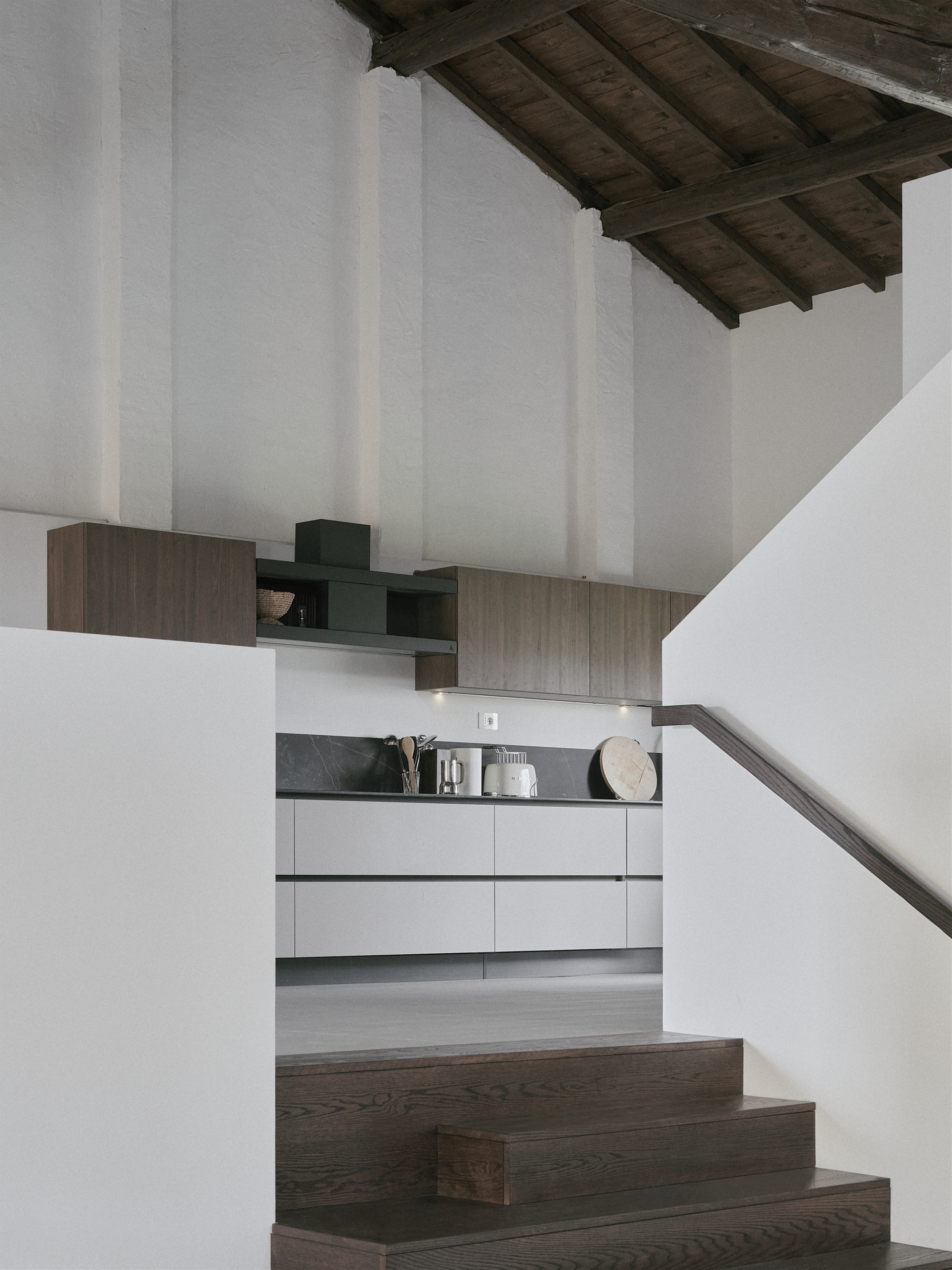 Kitchen glimpsed beyond timber staircase treads under the sloped wooden ceiling
