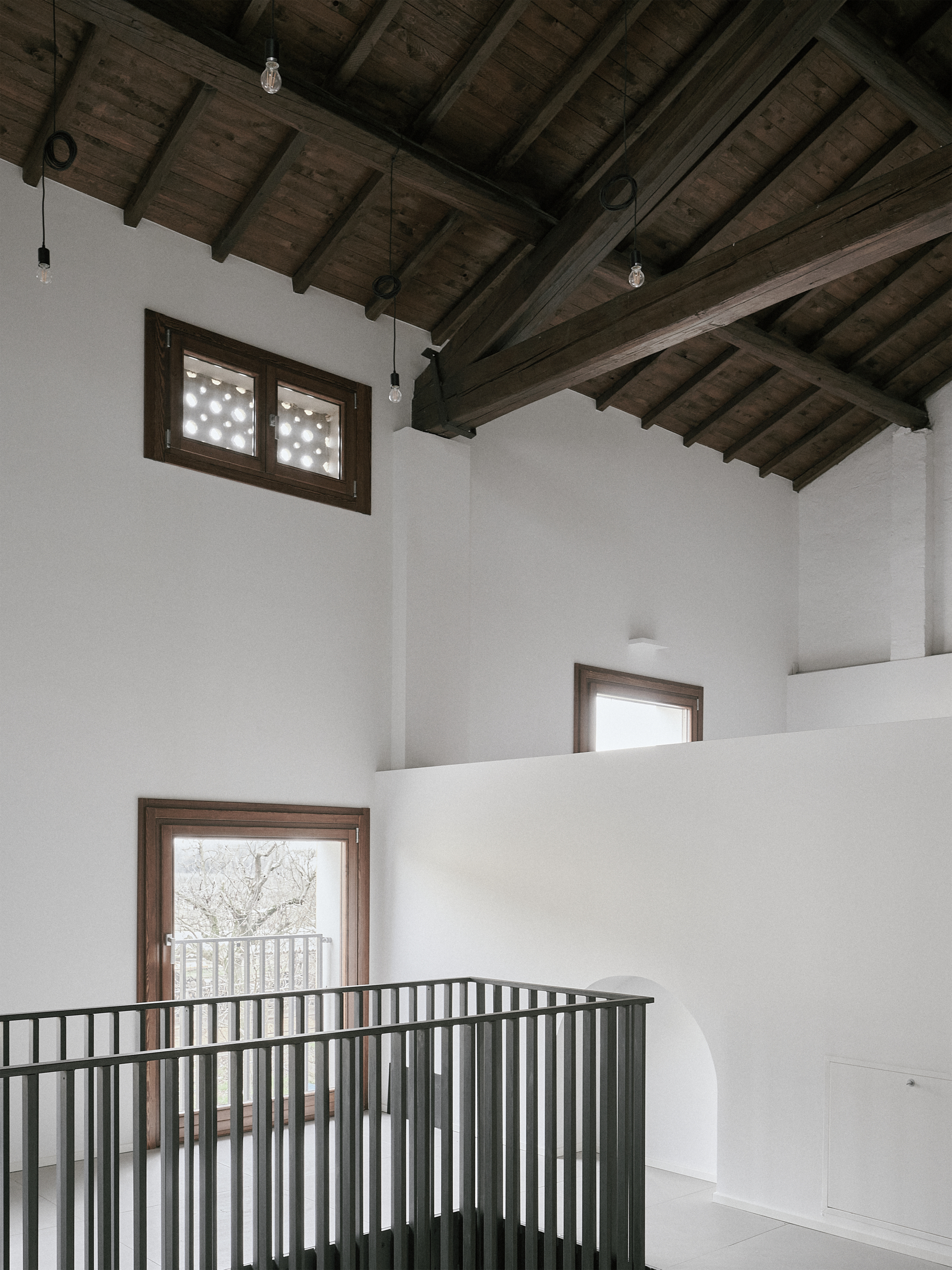 Double-height space with metal railing balcony and timber-framed windows overlooking bare winter trees