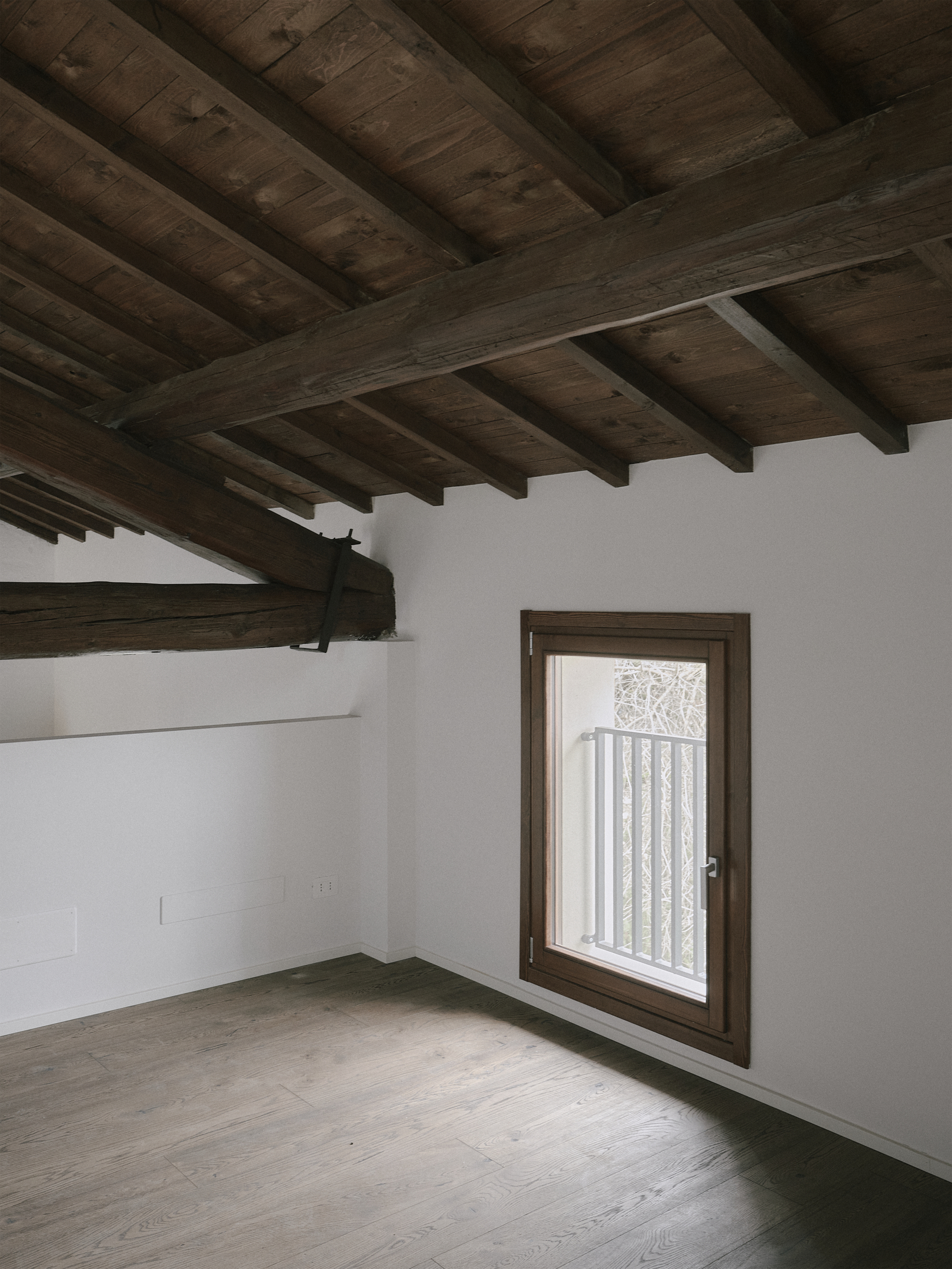 Timber-framed casement window in white plaster wall under exposed beam ceiling with concrete floor