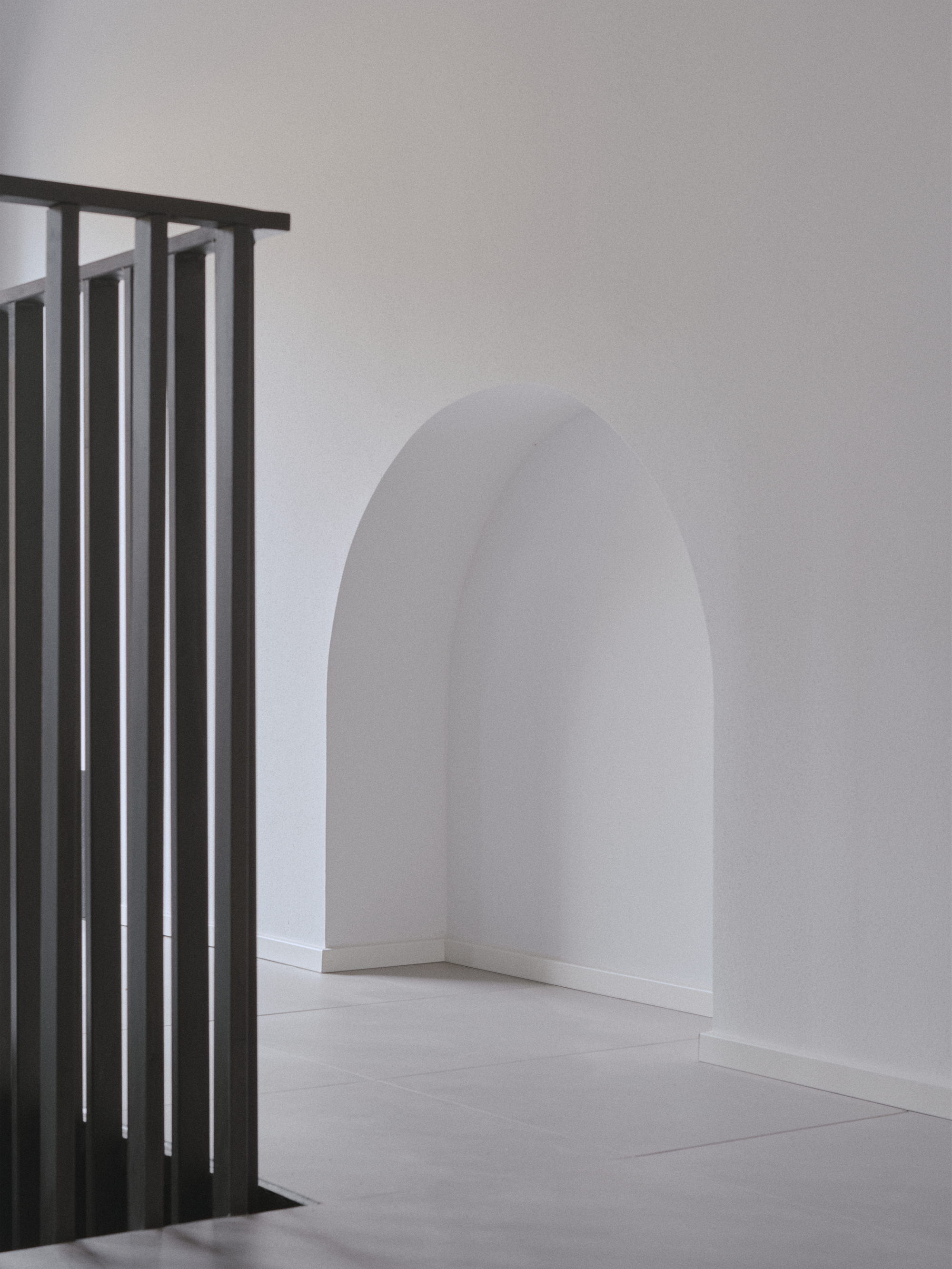 Metal slat balustrade beside an arched doorway with white plaster walls and pale flooring