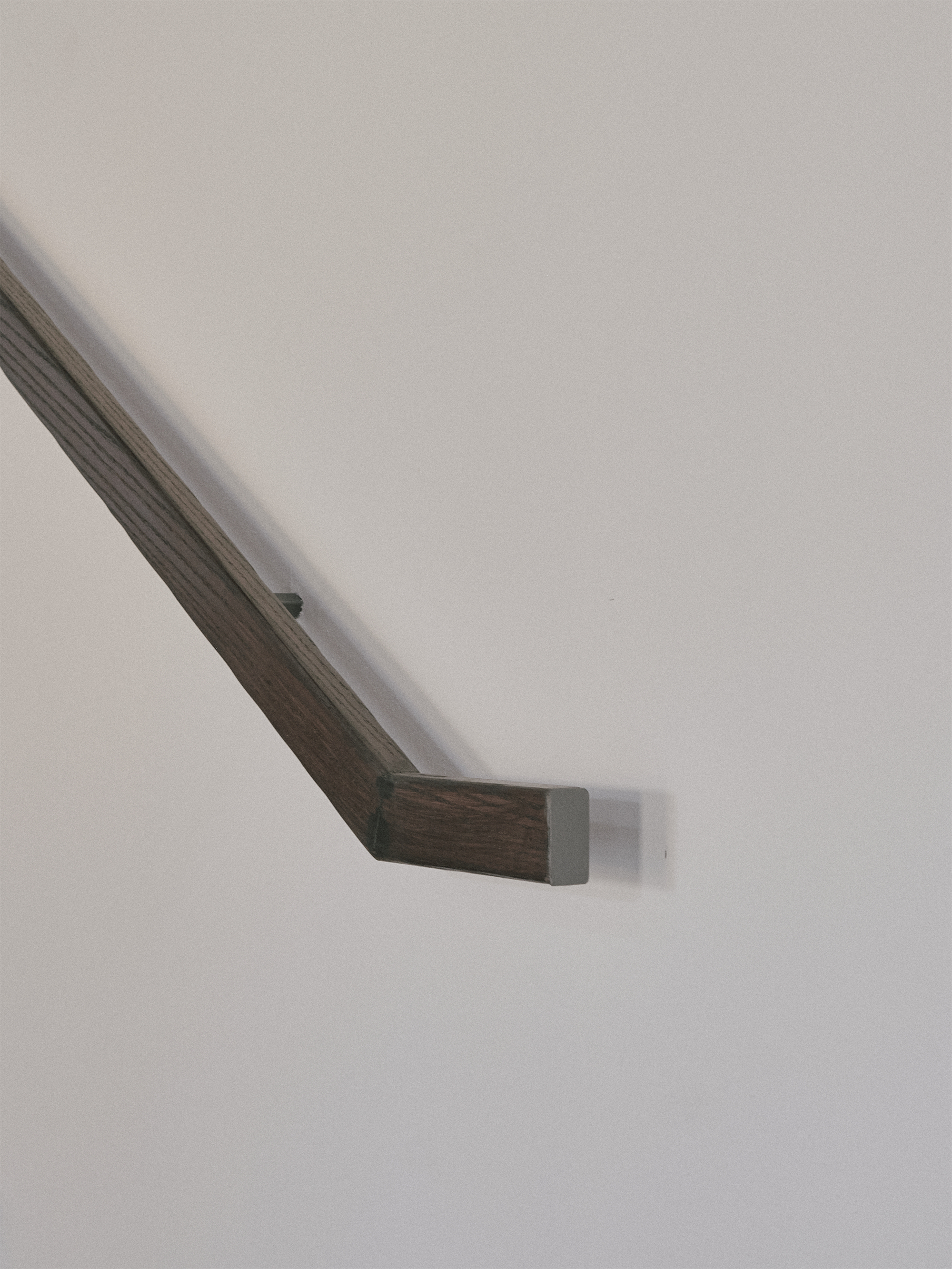 Close-up of a timber handrail with metal bracket mounting against a white wall