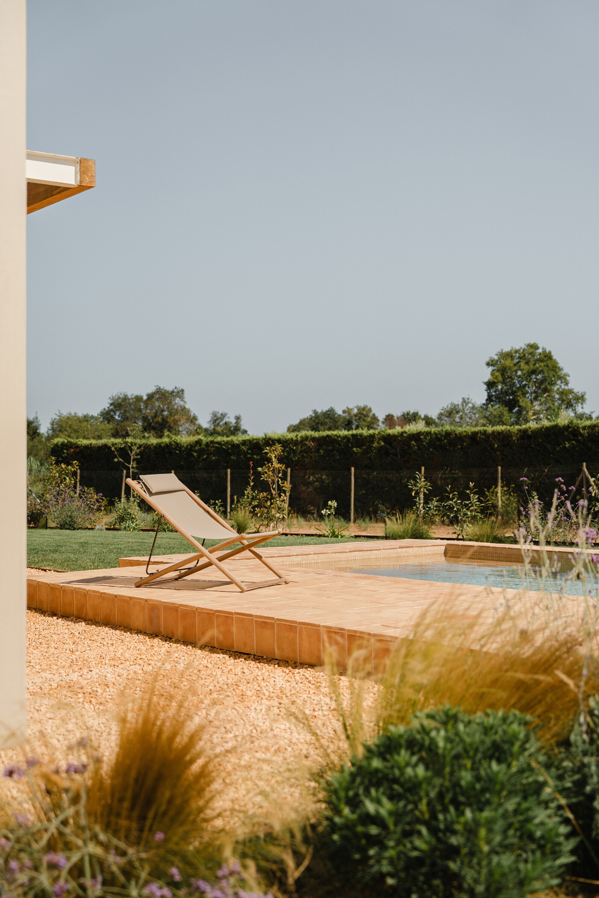 Timber deck terrace with canvas lounge chair beside gravel garden and hedgerow