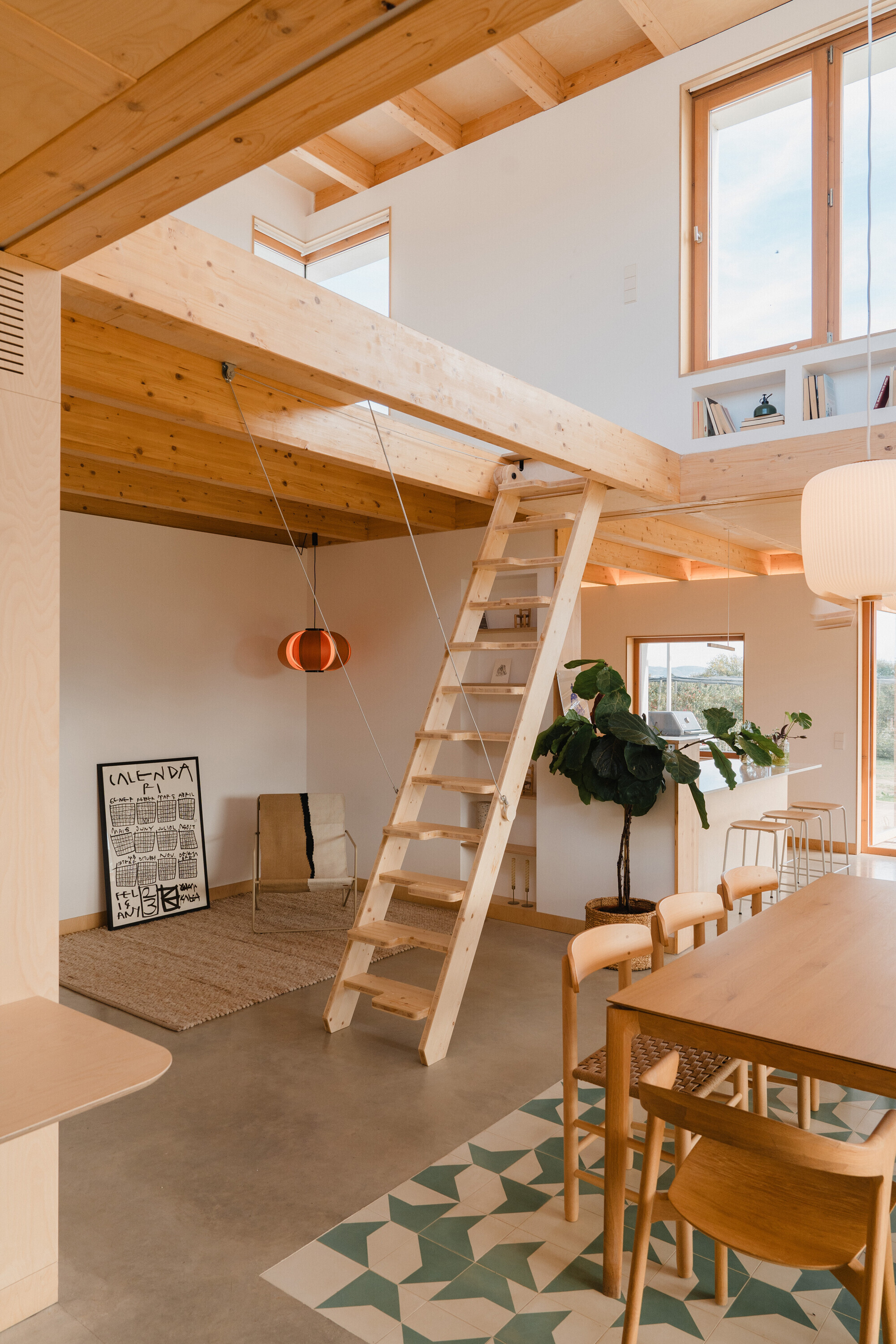 Double-height living space with timber ladder stair leading to upper mezzanine and geometric floor tiles beneath