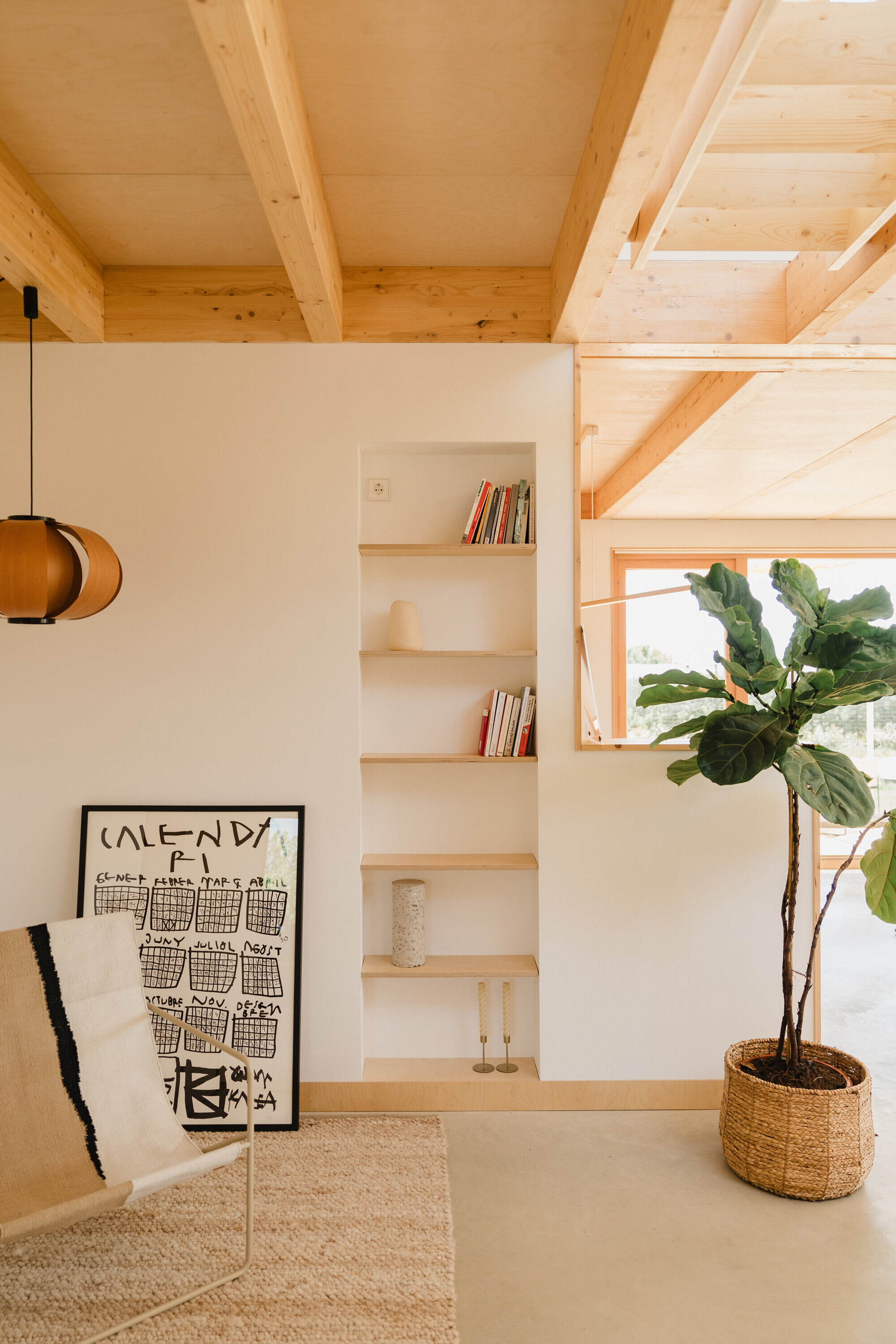 Built-in shelving unit beneath timber staircase with potted fiddle-leaf fig and pendant lamp overhead