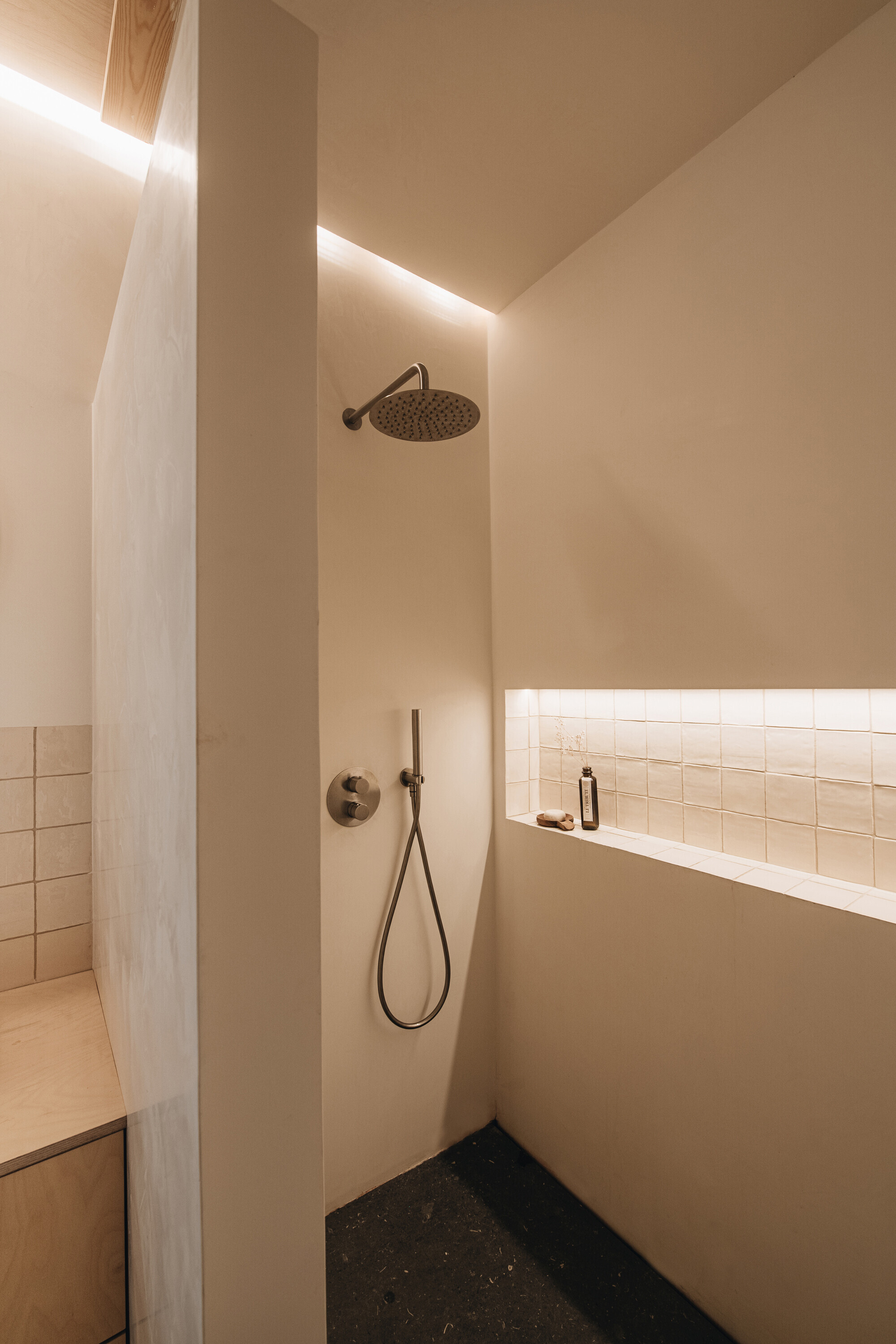 Shower corner with overhead rain fixture, polished plaster walls and concealed linear lighting at the ceiling