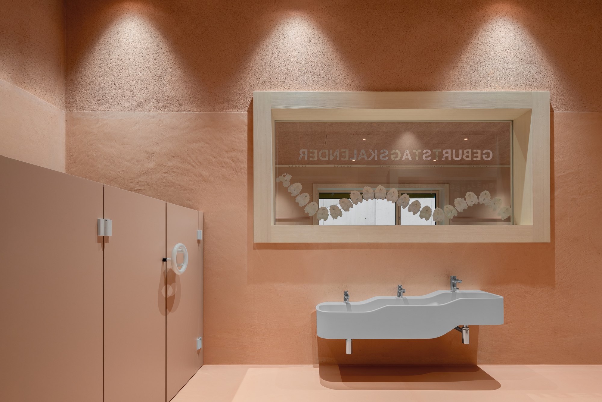 Washroom with triple-basin sink, terracotta walls, and illuminated window display showing paper cutouts above