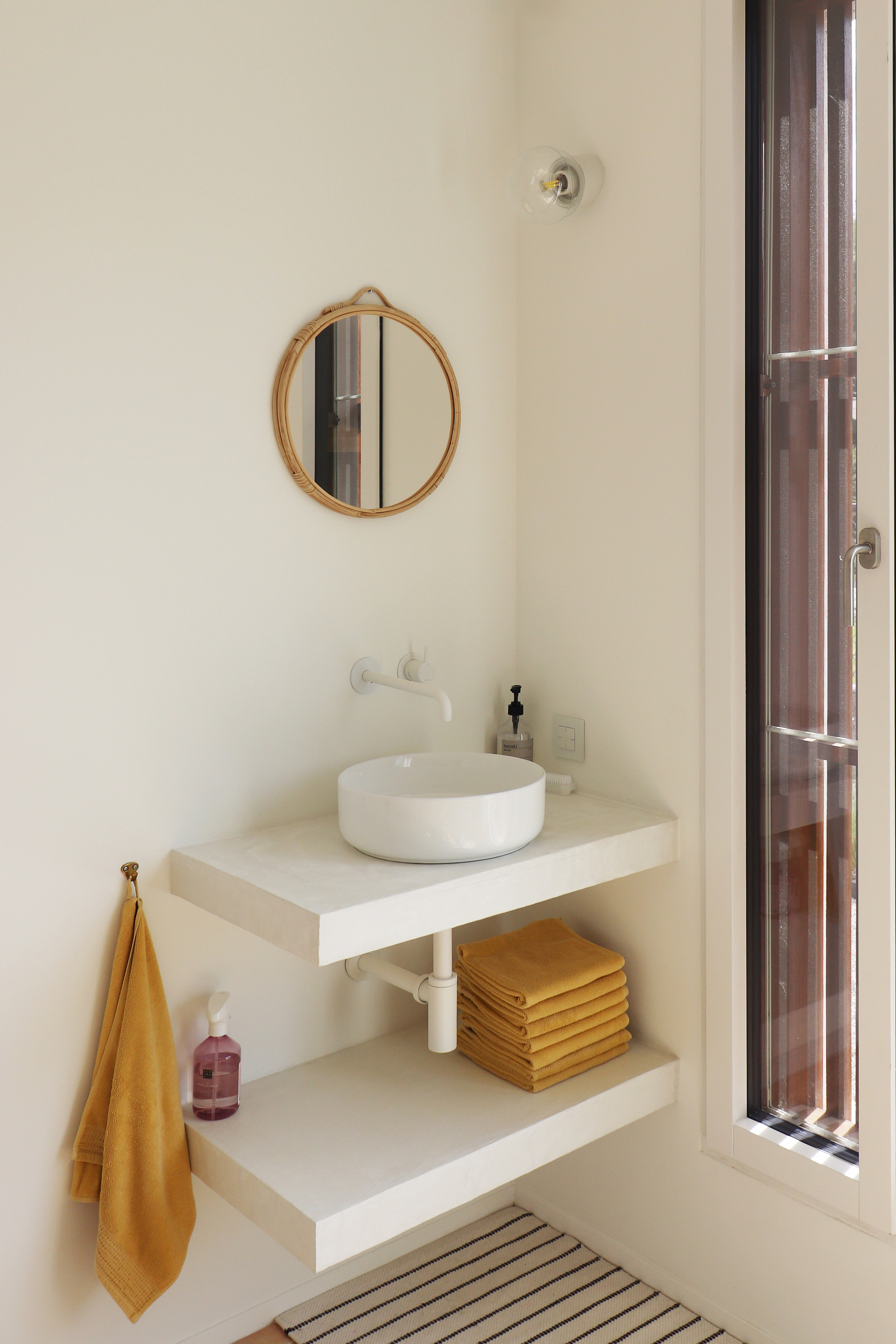 Bathroom vanity with floating shelves, round vessel sink, circular mirror and tall louvered wooden door