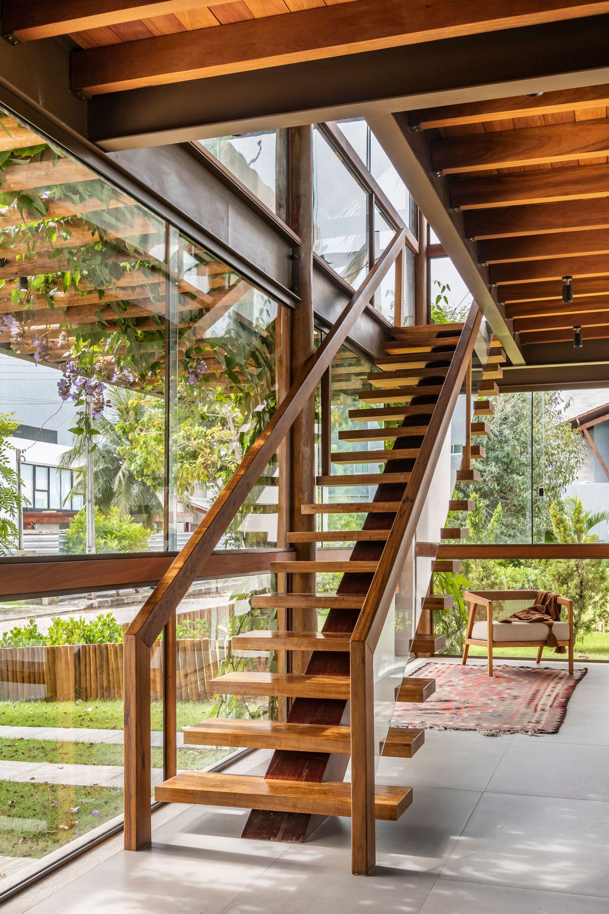 Open-tread timber staircase with diagonal structural bracing and glazed wall revealing the garden beyond