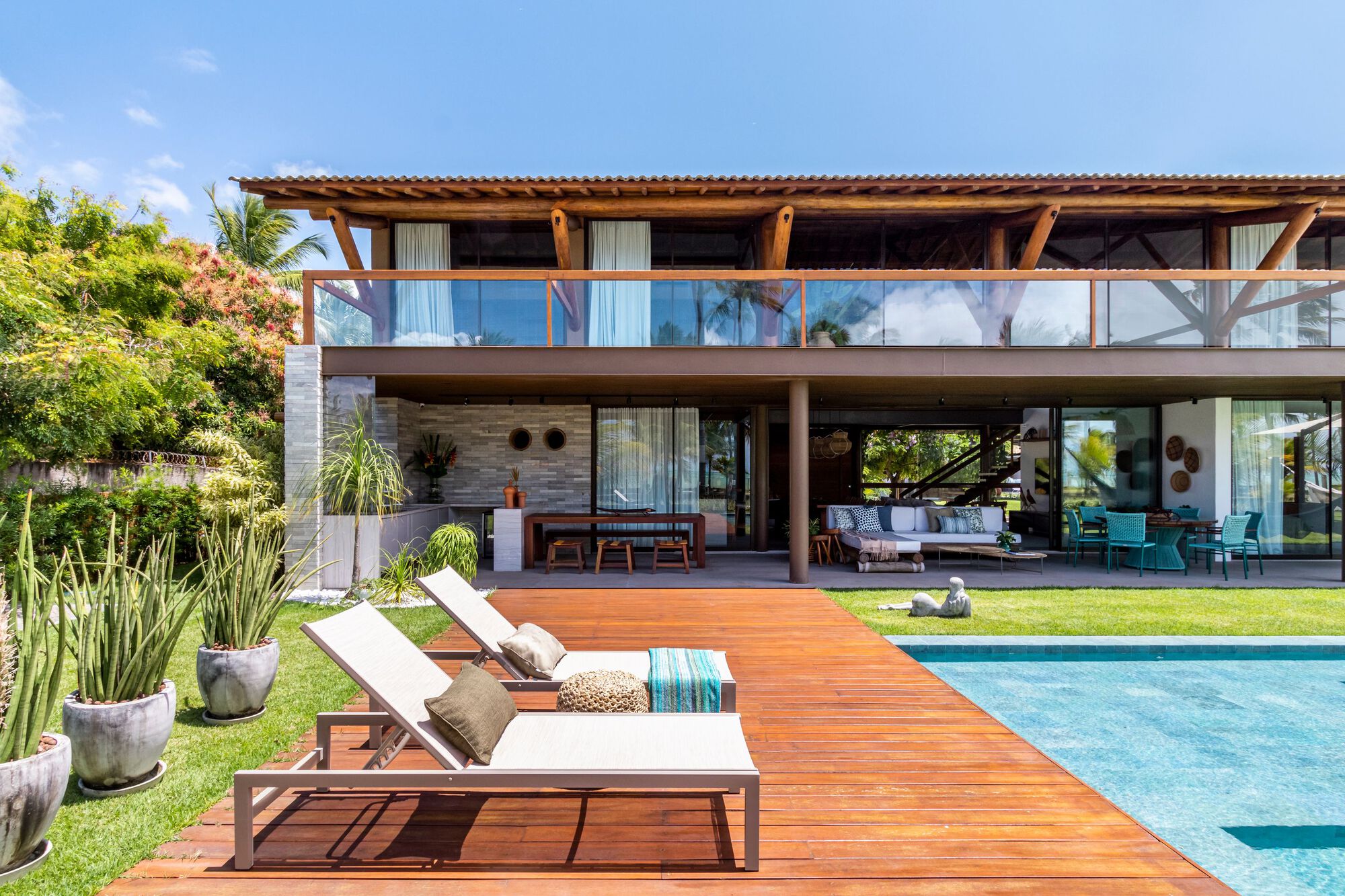Rear elevation showing timber deck extending from open living area toward swimming pool under clear sky
