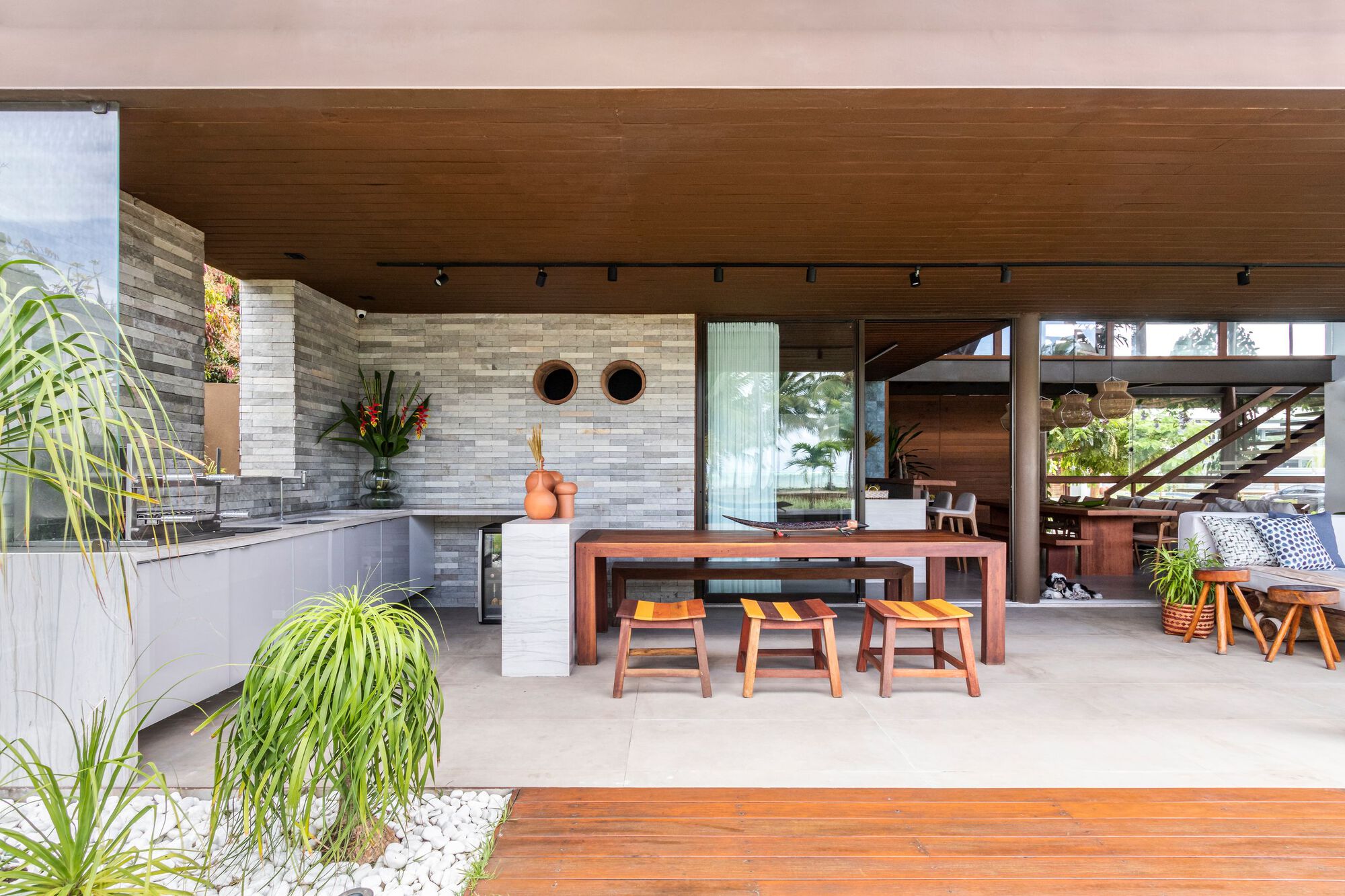 Covered outdoor dining terrace with timber ceiling, stacked stone wall and views into interior living space