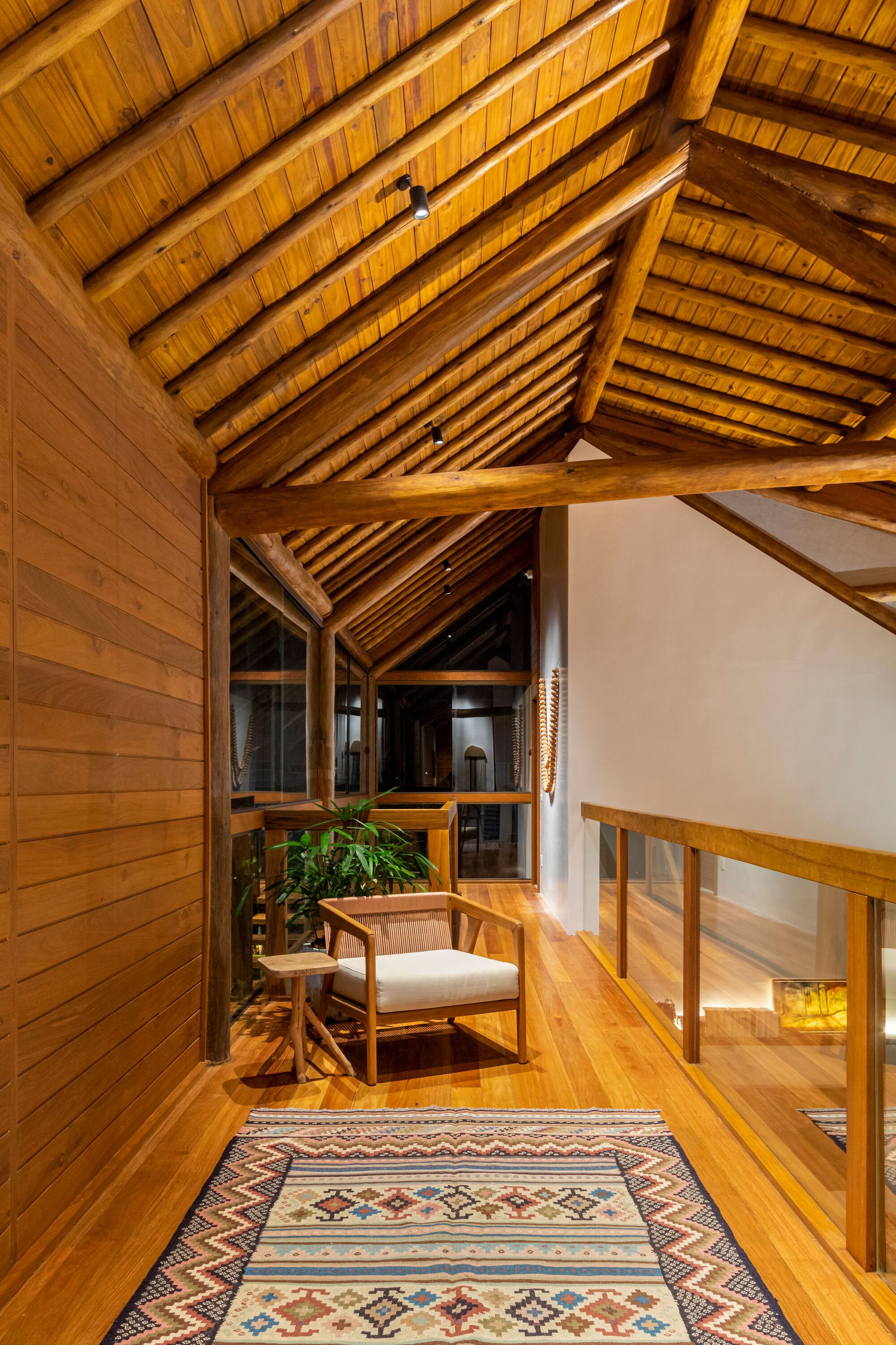 Upper hallway with exposed timber rafters and planked ceiling above a patterned rug
