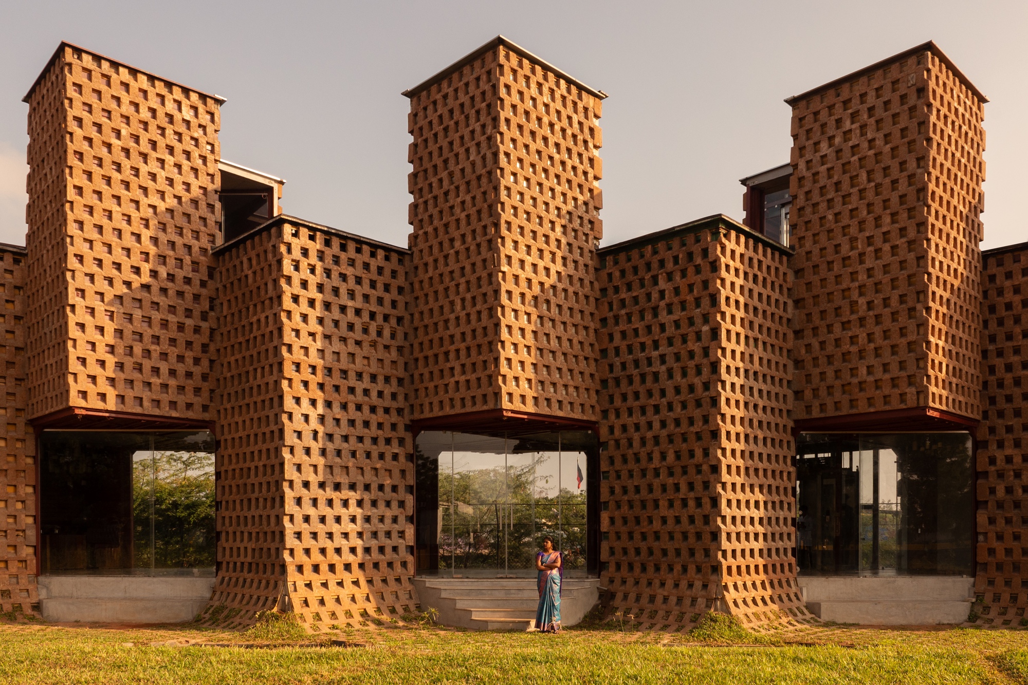 Rhythmic brick piers with staggered openings forming arched passageways at ground level at dusk