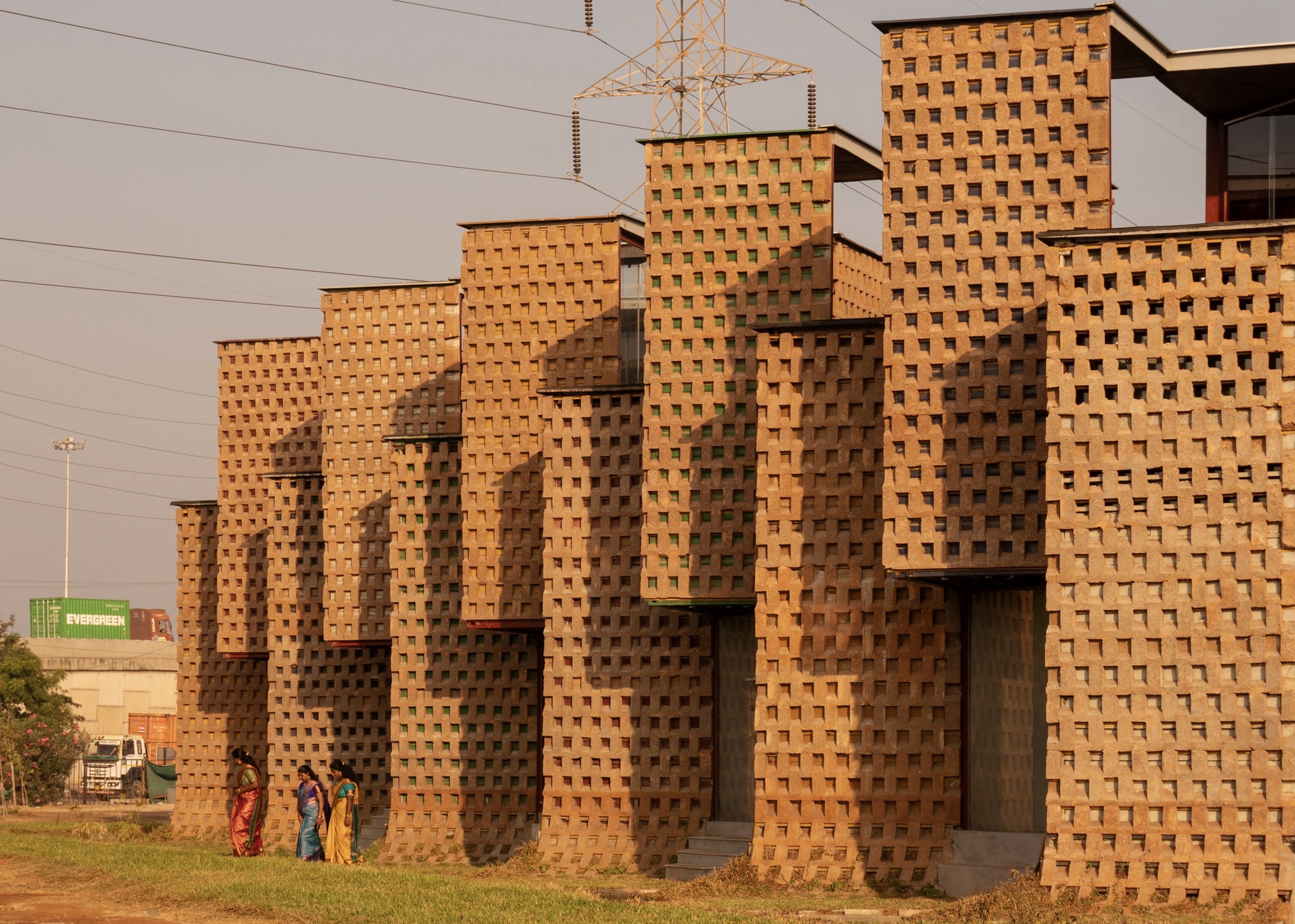 Oblique view of the stepped brick facade with transmission towers visible beyond at golden hour