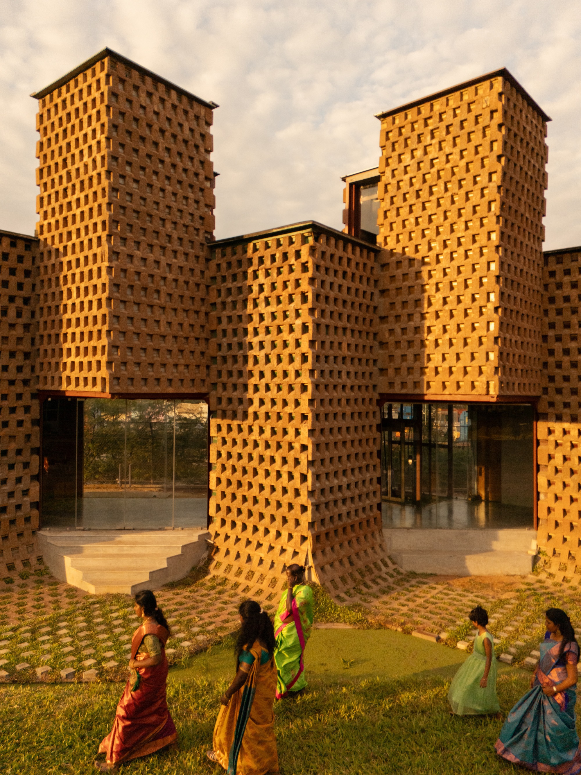 Entrance view of tapered perforated brick towers in warm evening light with visitors gathered below