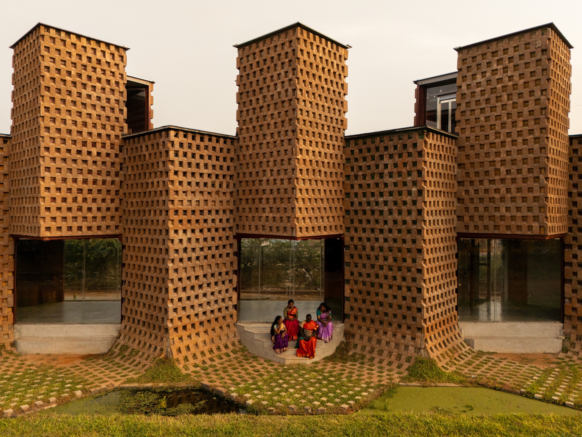 Symmetrical facade of perforated brick columns with glass entrances and visitors in shadow beneath curved canopy