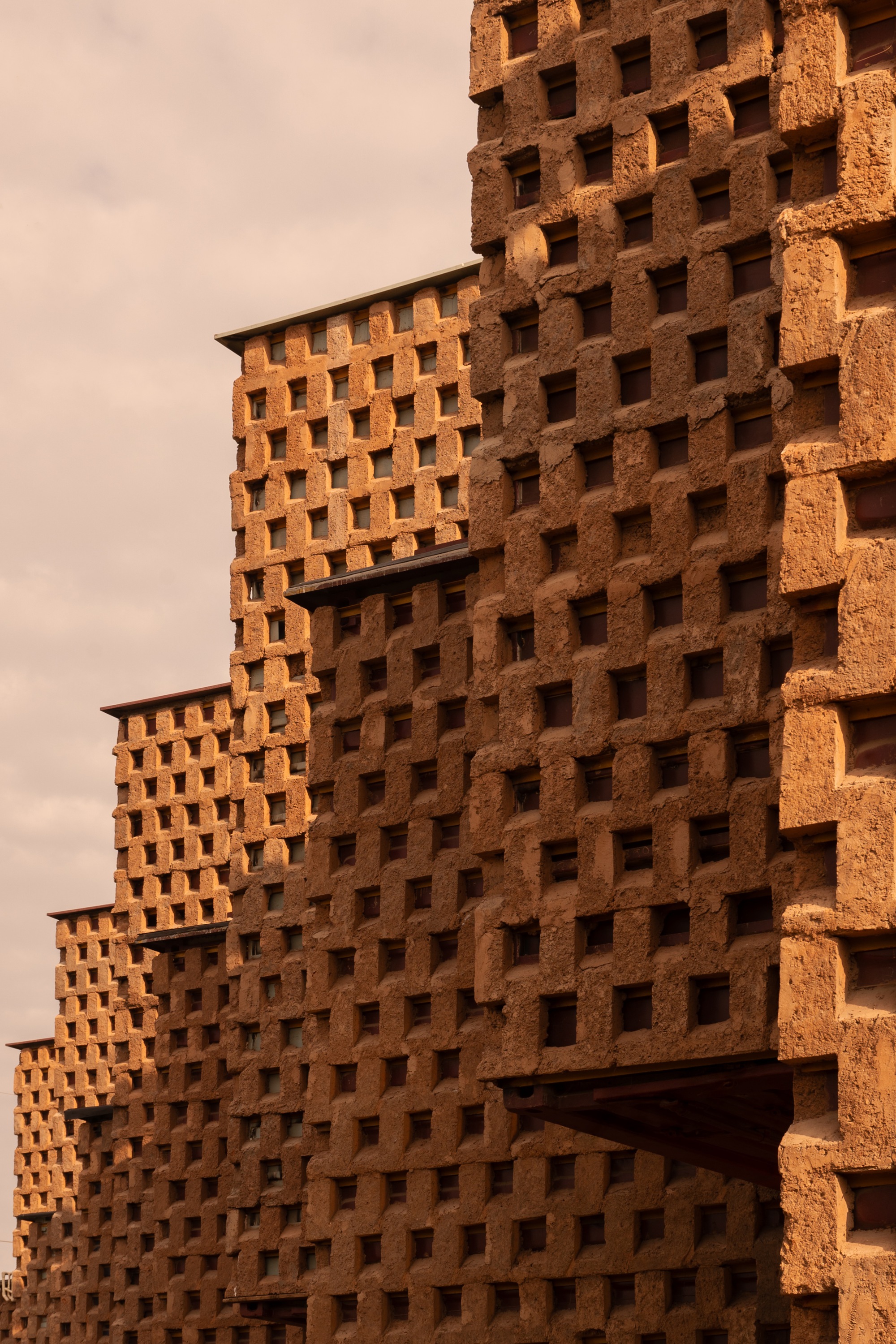 Close-up of the perforated terracotta brick facade with interlocking volumes under warm afternoon light