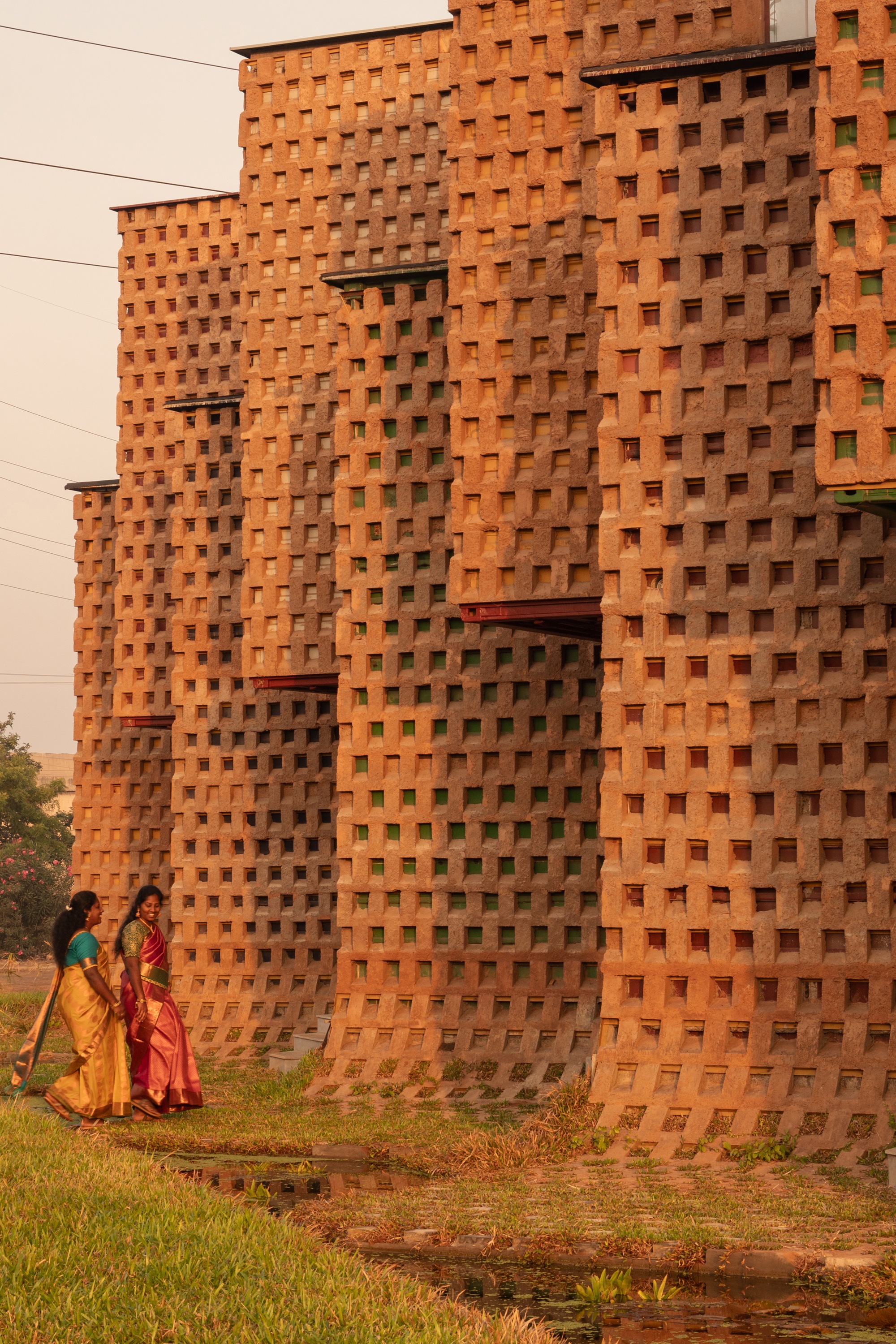 Perforated terracotta brick wall with two figures in traditional dress walking on adjacent grass