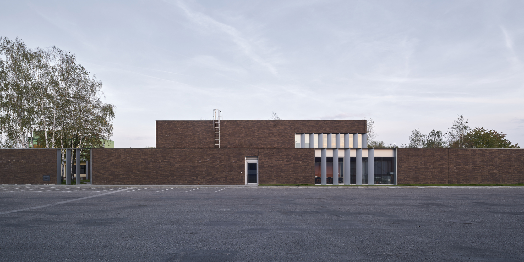 Long dark brick facade with vertical window openings across an empty asphalt forecourt