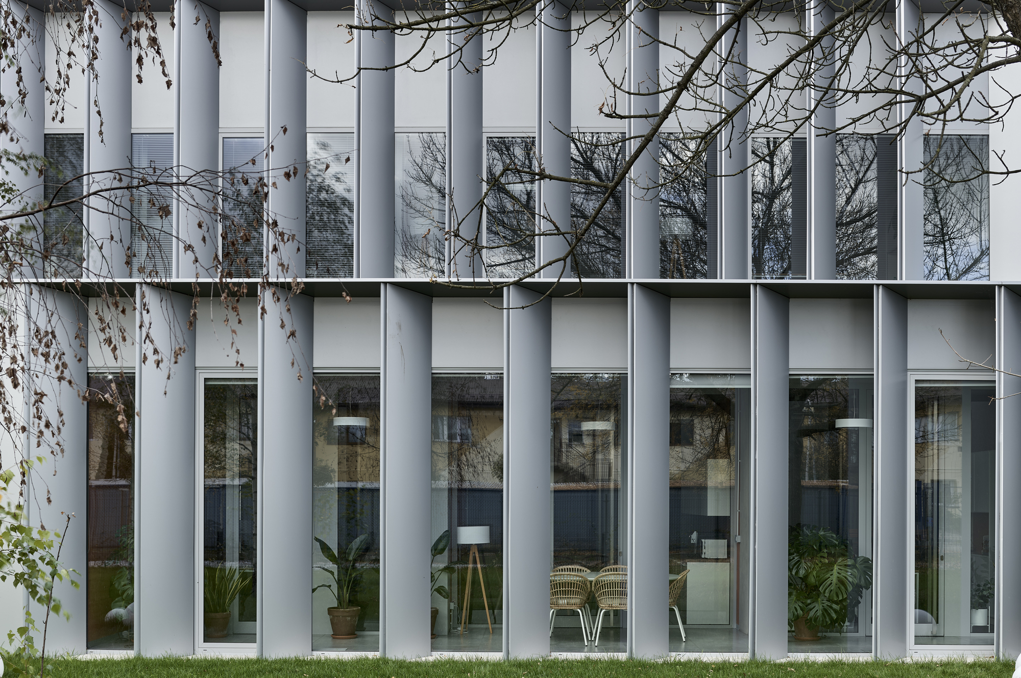Close-up of the white vertical fin facade with alternating glazed openings reflecting bare branches