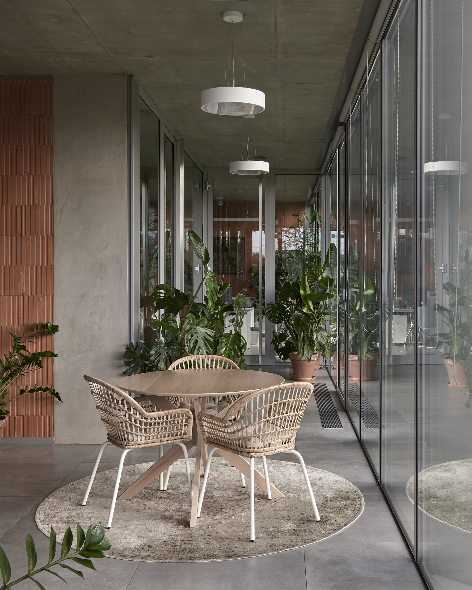 Covered terrace with rattan dining set and potted plants flanked by floor-to-ceiling glazing and timber slat wall