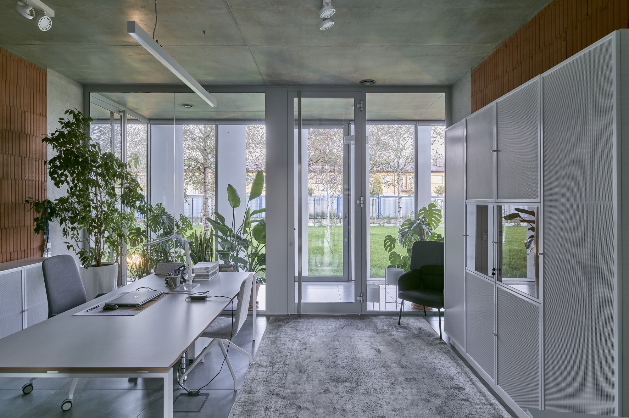 Office interior with white workstations and storage wall facing glazed doors opening to lawn and trees