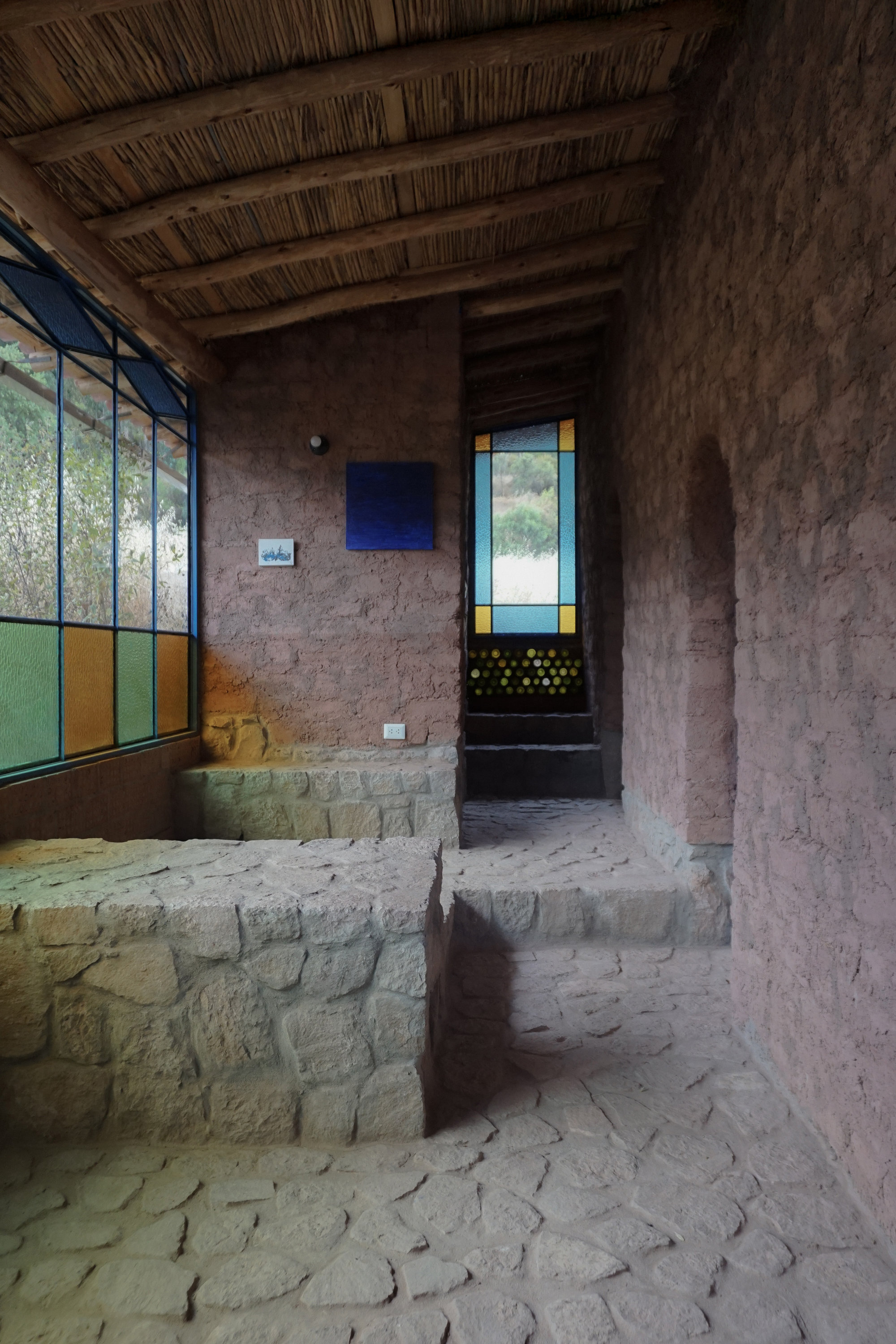 Interior room with exposed reed ceiling, adobe walls, and multi-colored glazed window panels