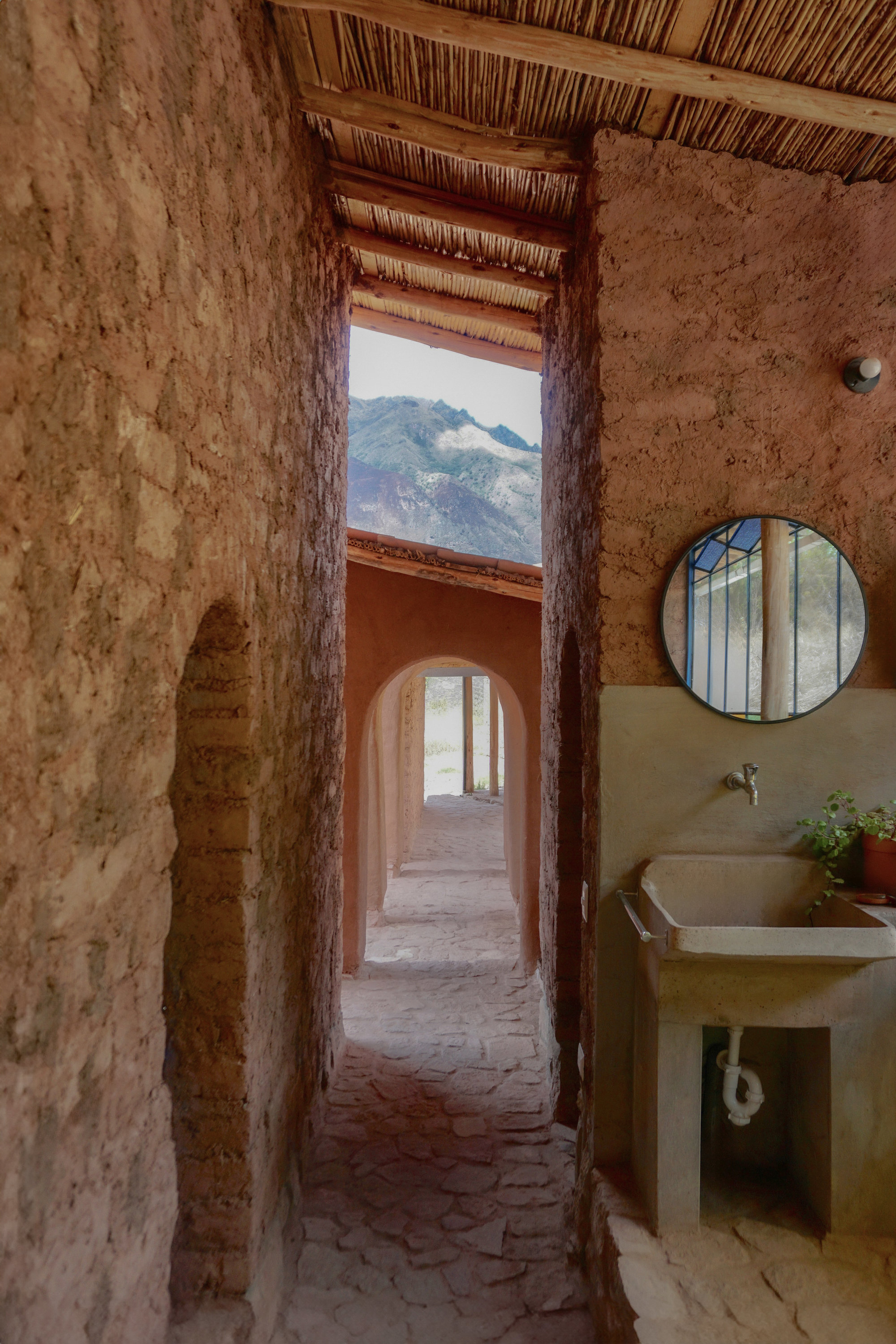 Bathroom interior with sink and round mirror beneath reed ceiling opening to mountain view