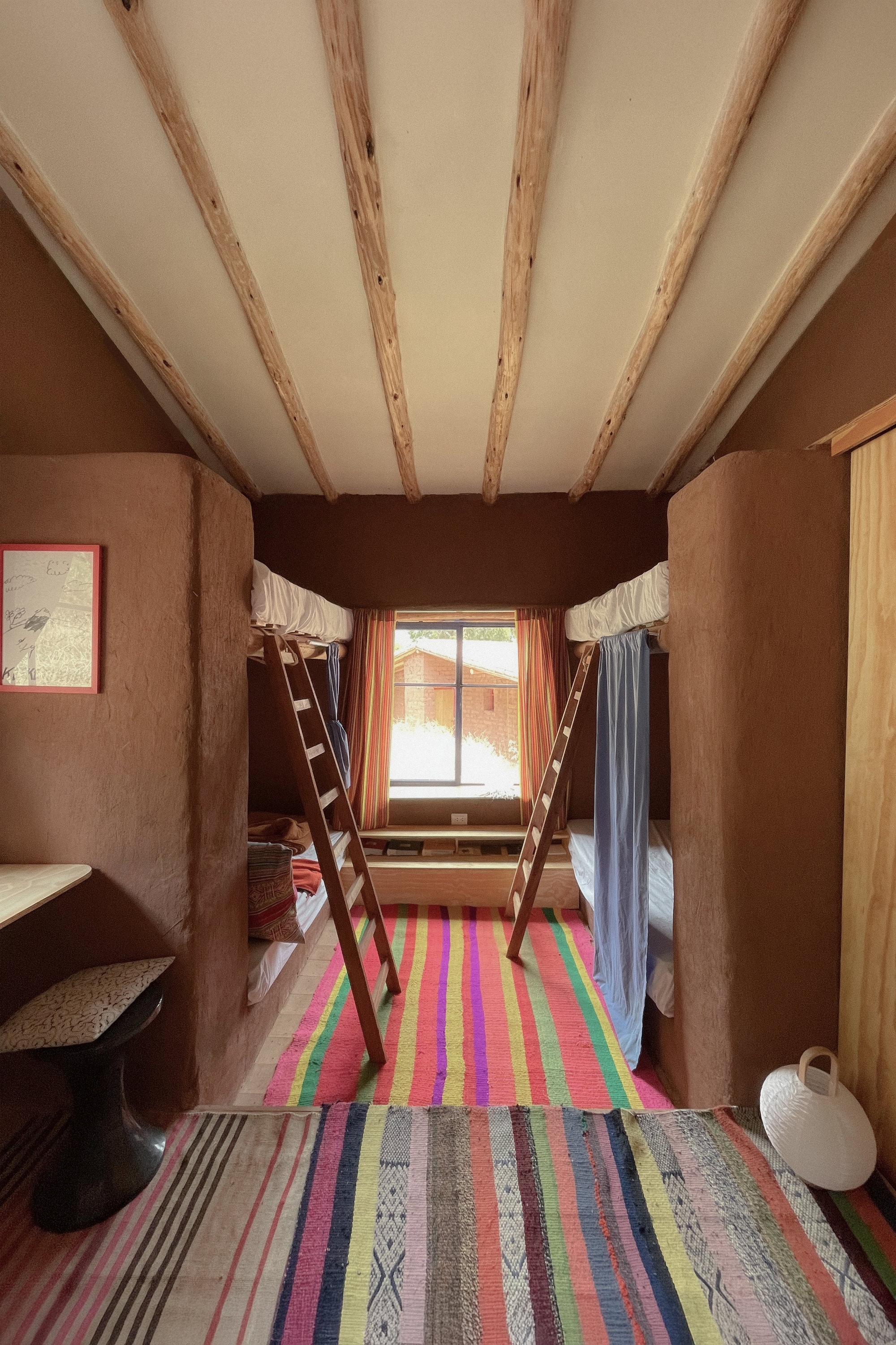 Sleeping room with exposed timber ceiling beams and striped textile rugs beneath twin ladder bunks