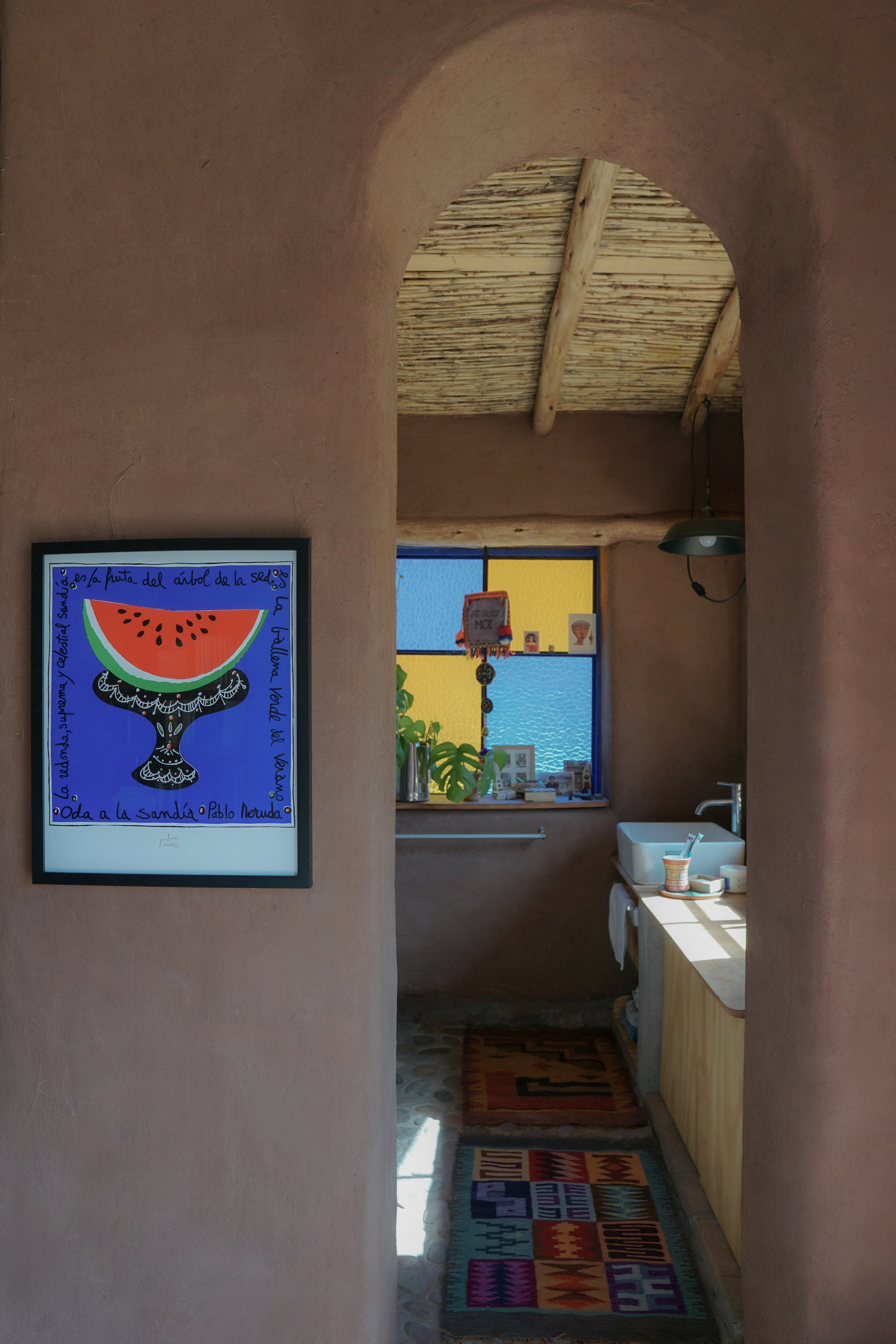 View through an arched doorway into a bathroom with bamboo ceiling and colored glass window over the tub