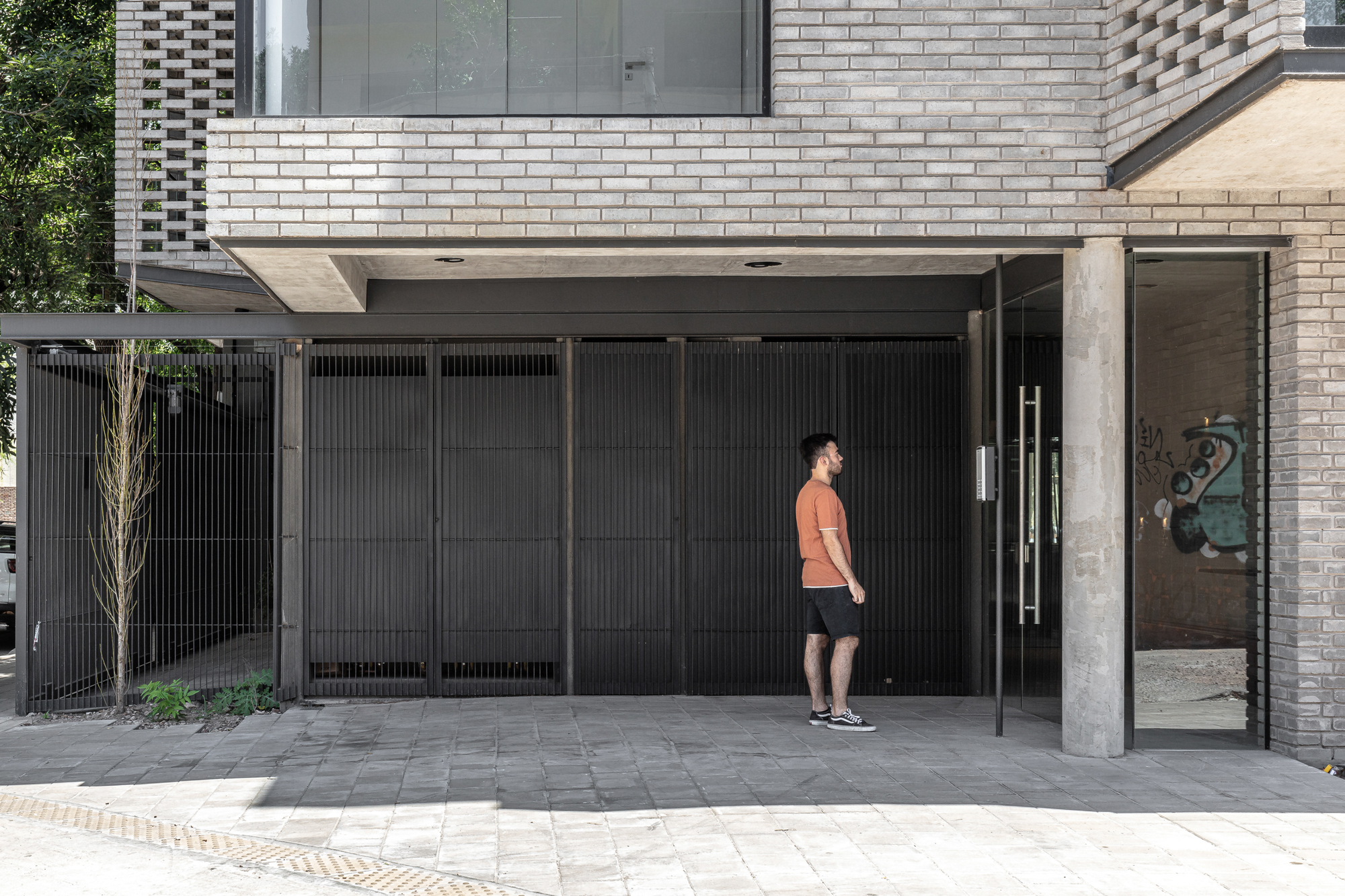 Ground-level entrance with black metal gate and person approaching under brick overhang