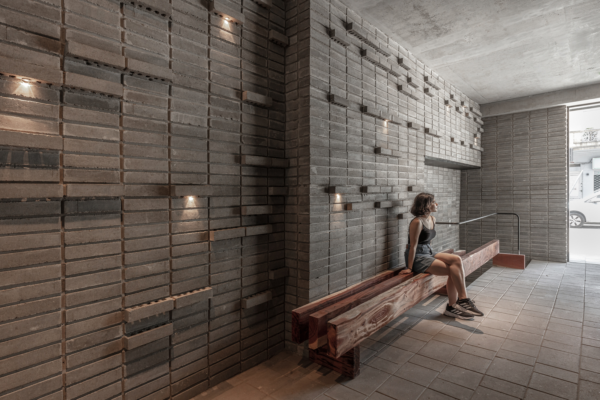 Entry vestibule with stacked brick screen walls and a person seated on a timber bench
