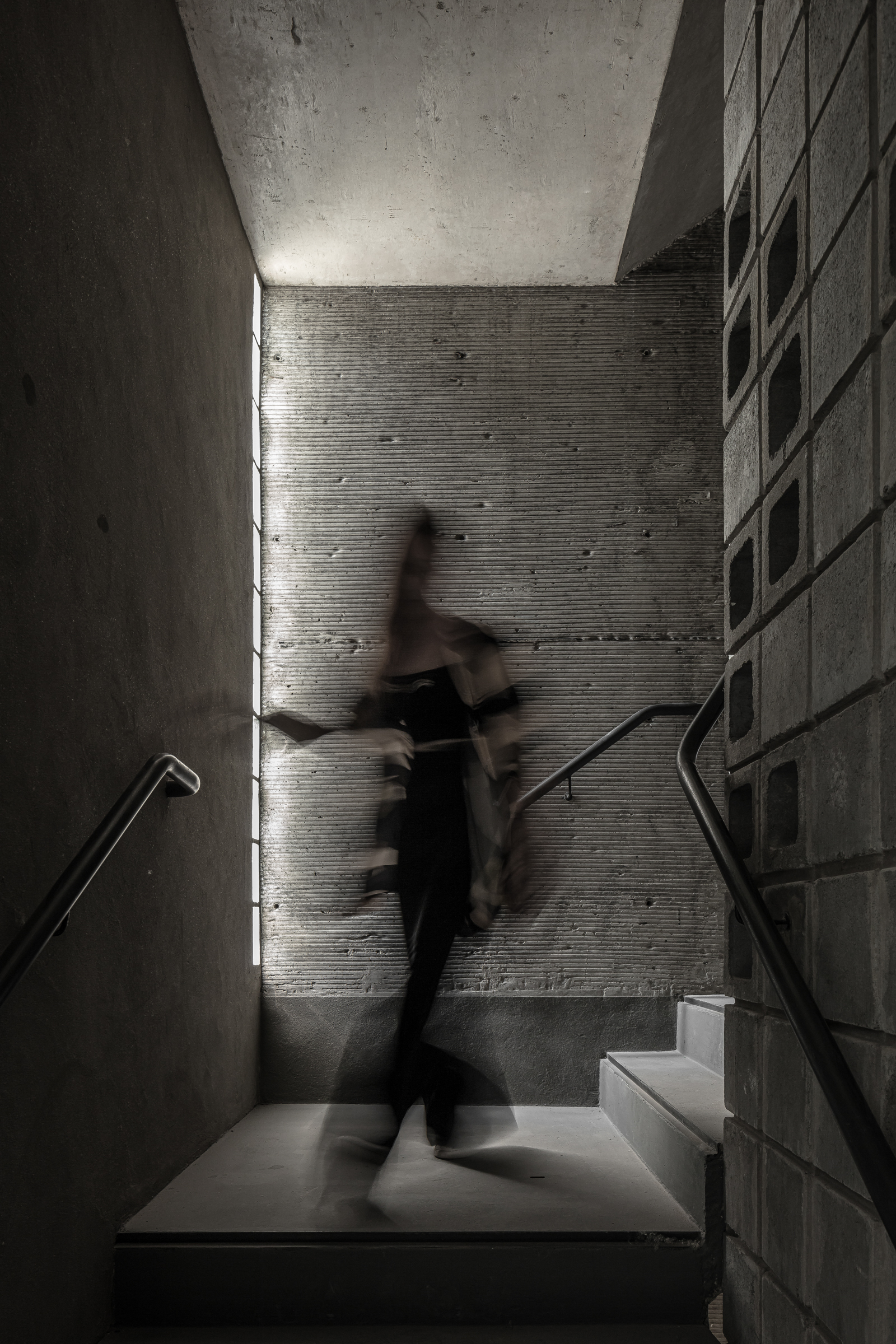 Concrete staircase landing with a figure in motion caught in daylight from a vertical slot window