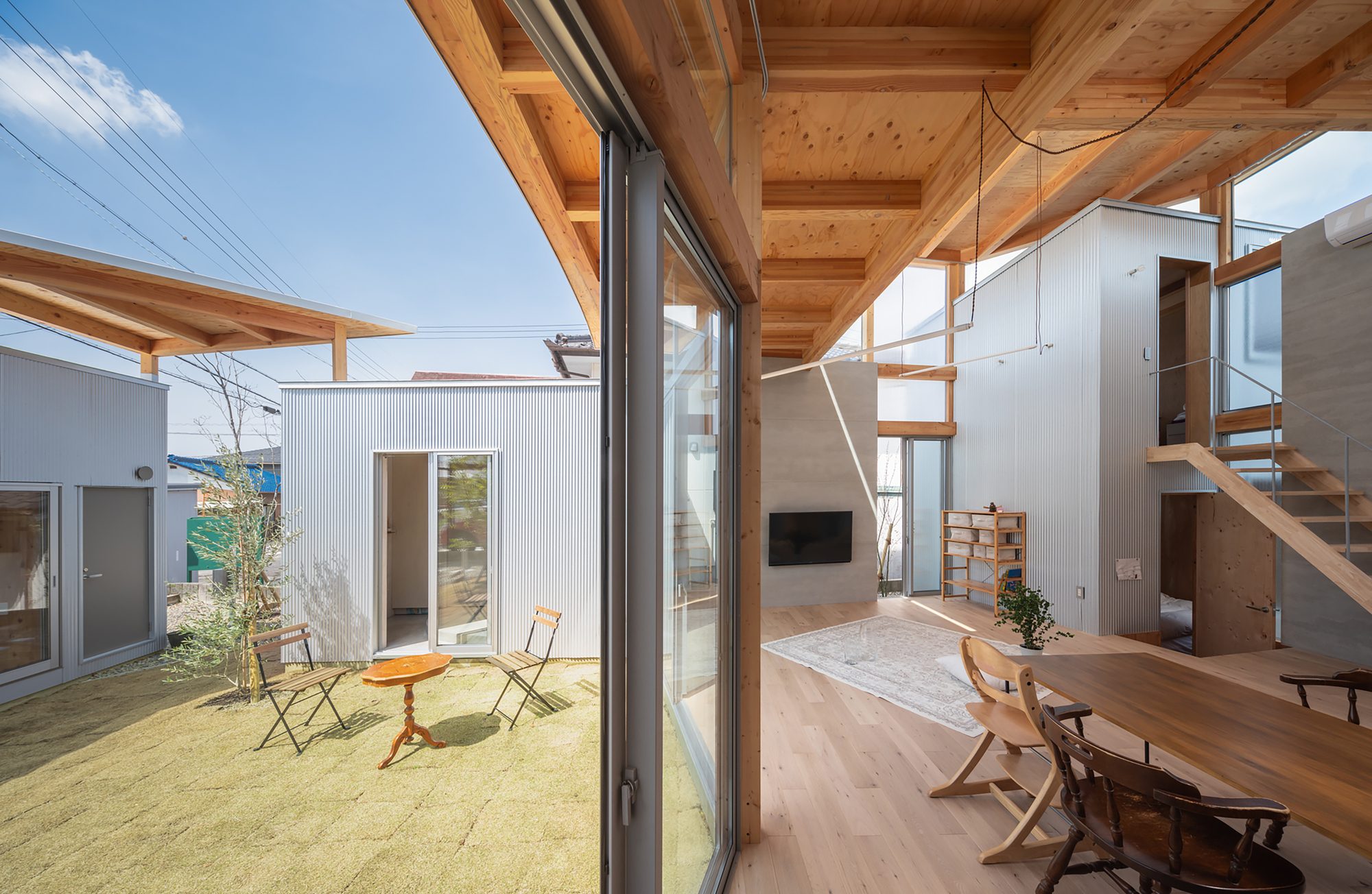 View through sliding glass doors toward a sand-filled courtyard with corrugated metal clad volumes beyond