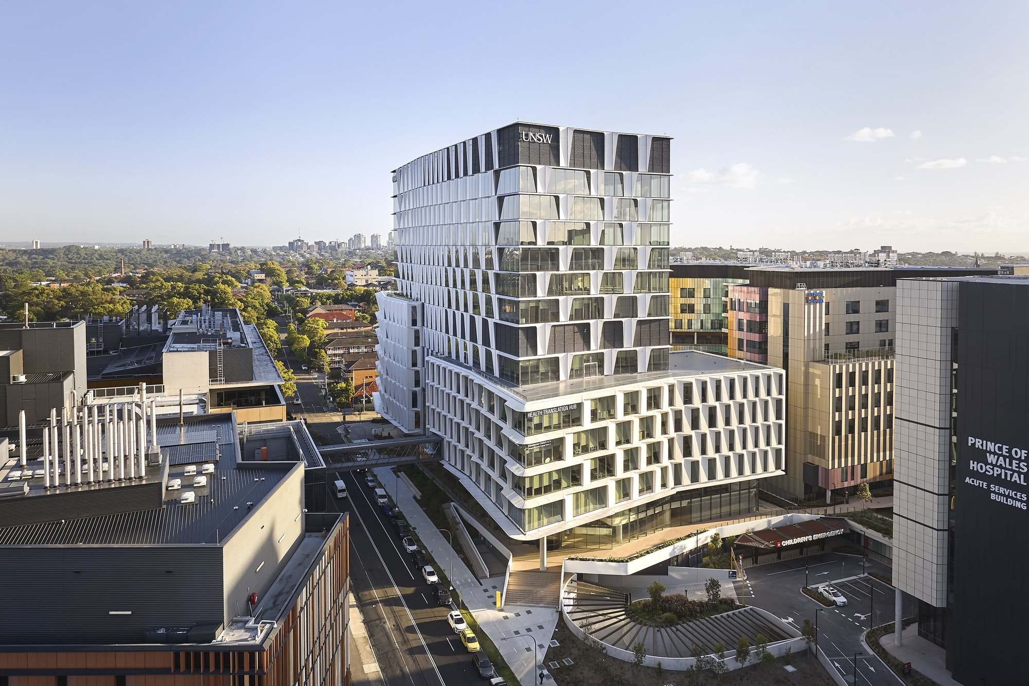 Aerial view of the stacked offset facade rising above surrounding rooftops and tree-lined streets