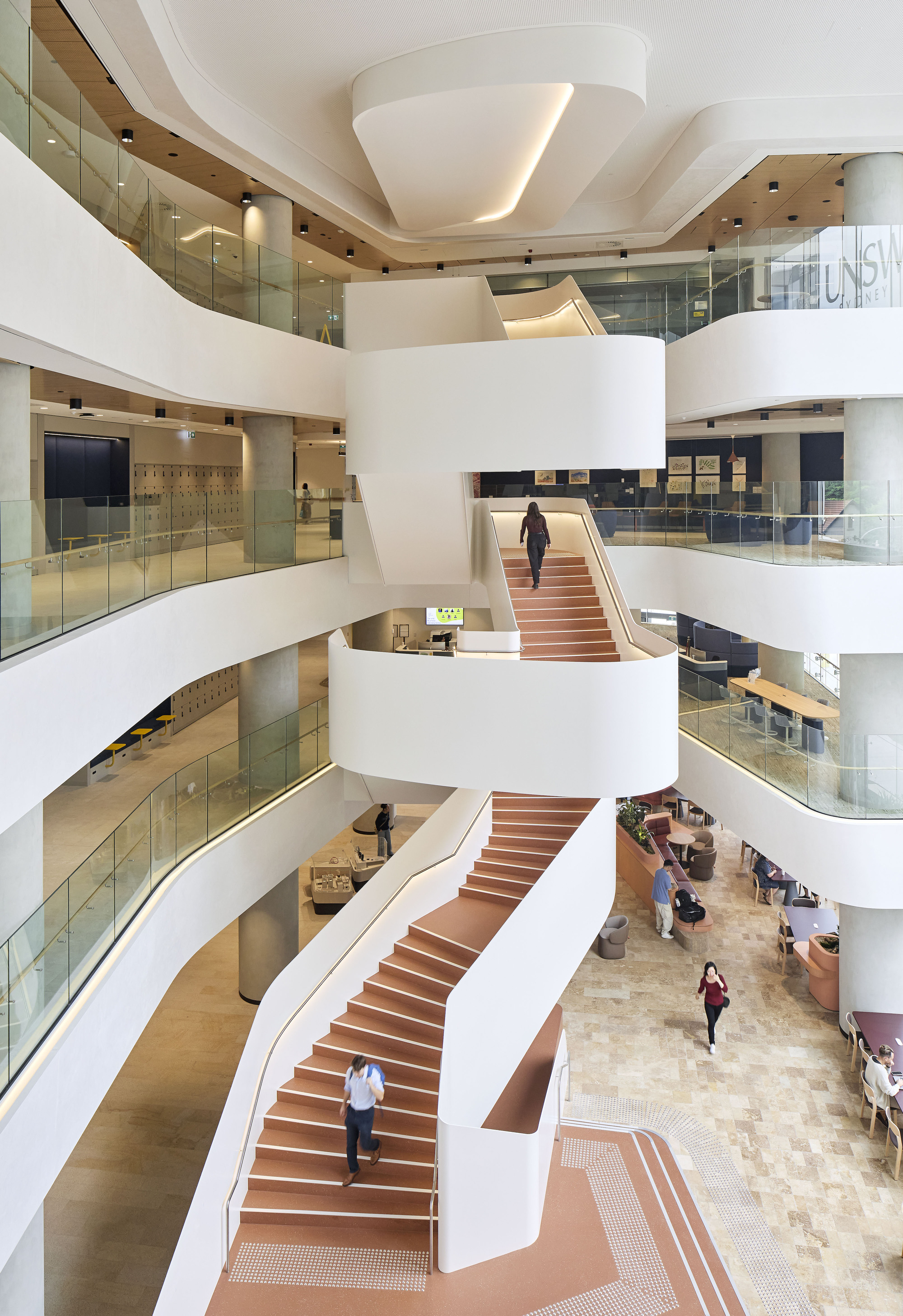 Multi-story atrium with interconnected timber-clad staircases and glass balustrades overlooking the ground floor