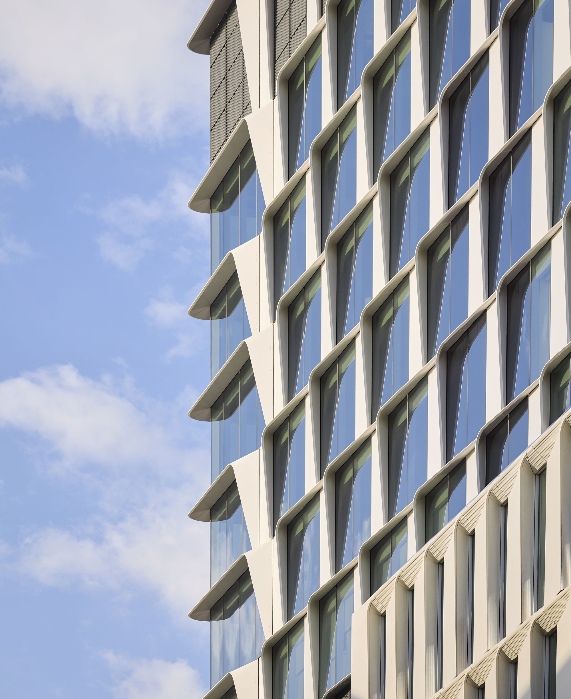 Oblique view of the alternating glass and concrete facade against scattered clouds