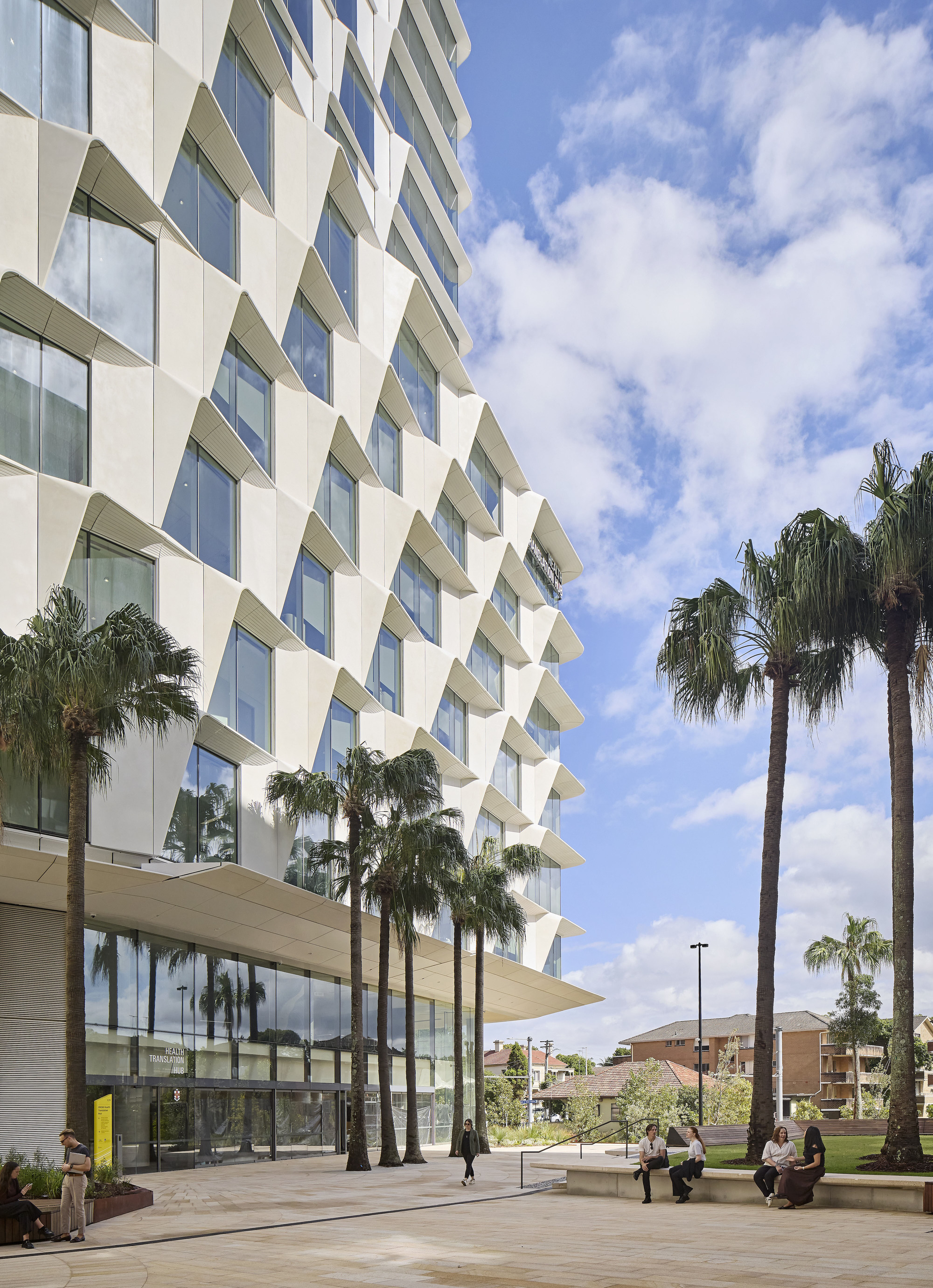 Sawtooth facade profile with alternating glass and white panels alongside palm trees and a plaza