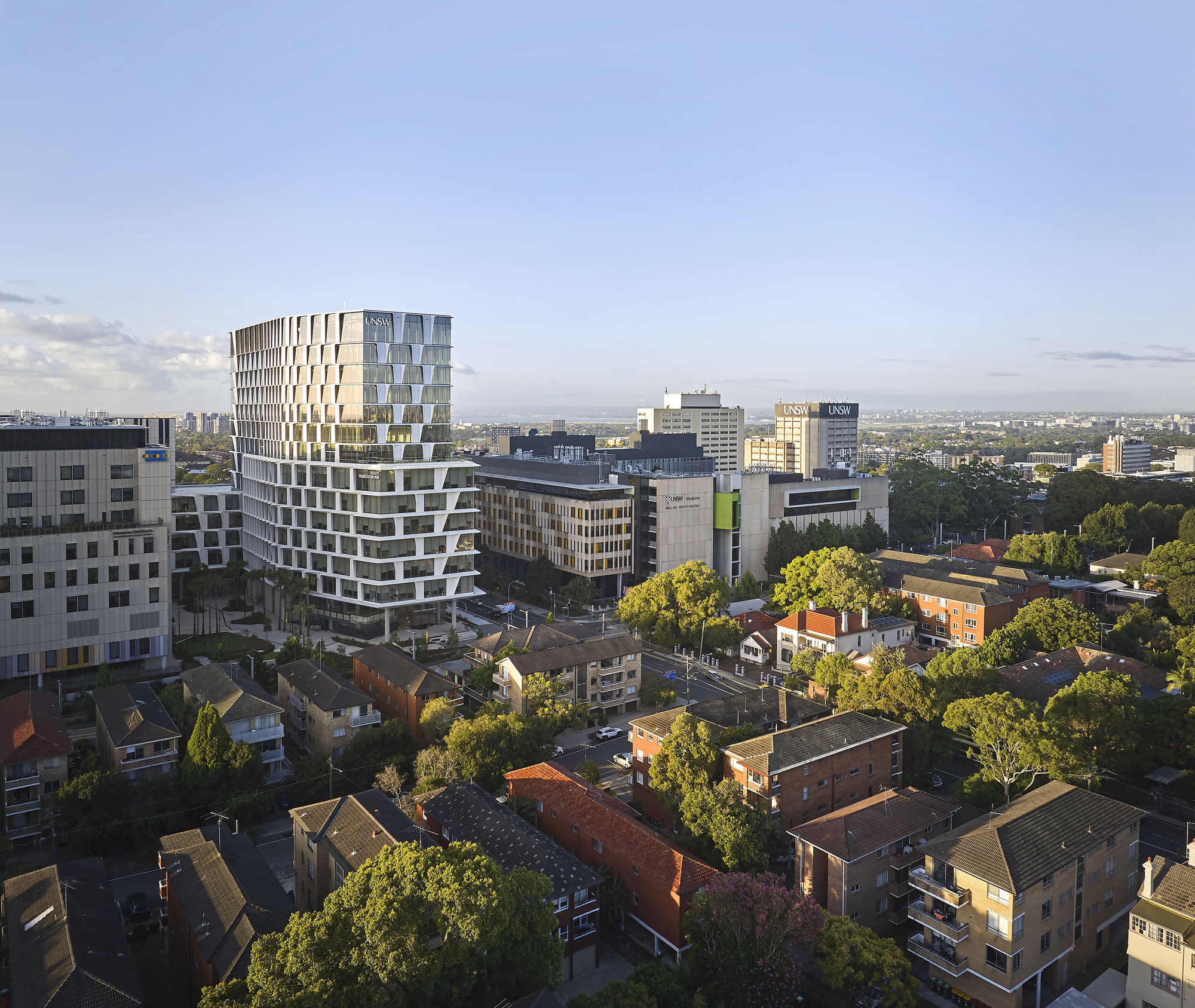 The stepped facade with offset balconies viewed from above at dusk over suburban rooftops