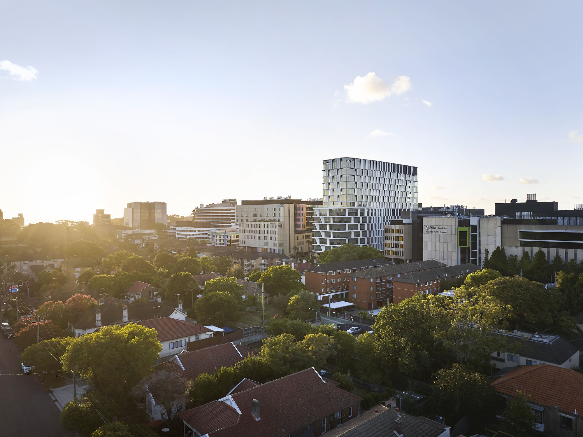 Tower with protruding floor plates visible in warm evening light across low-rise residential neighborhood