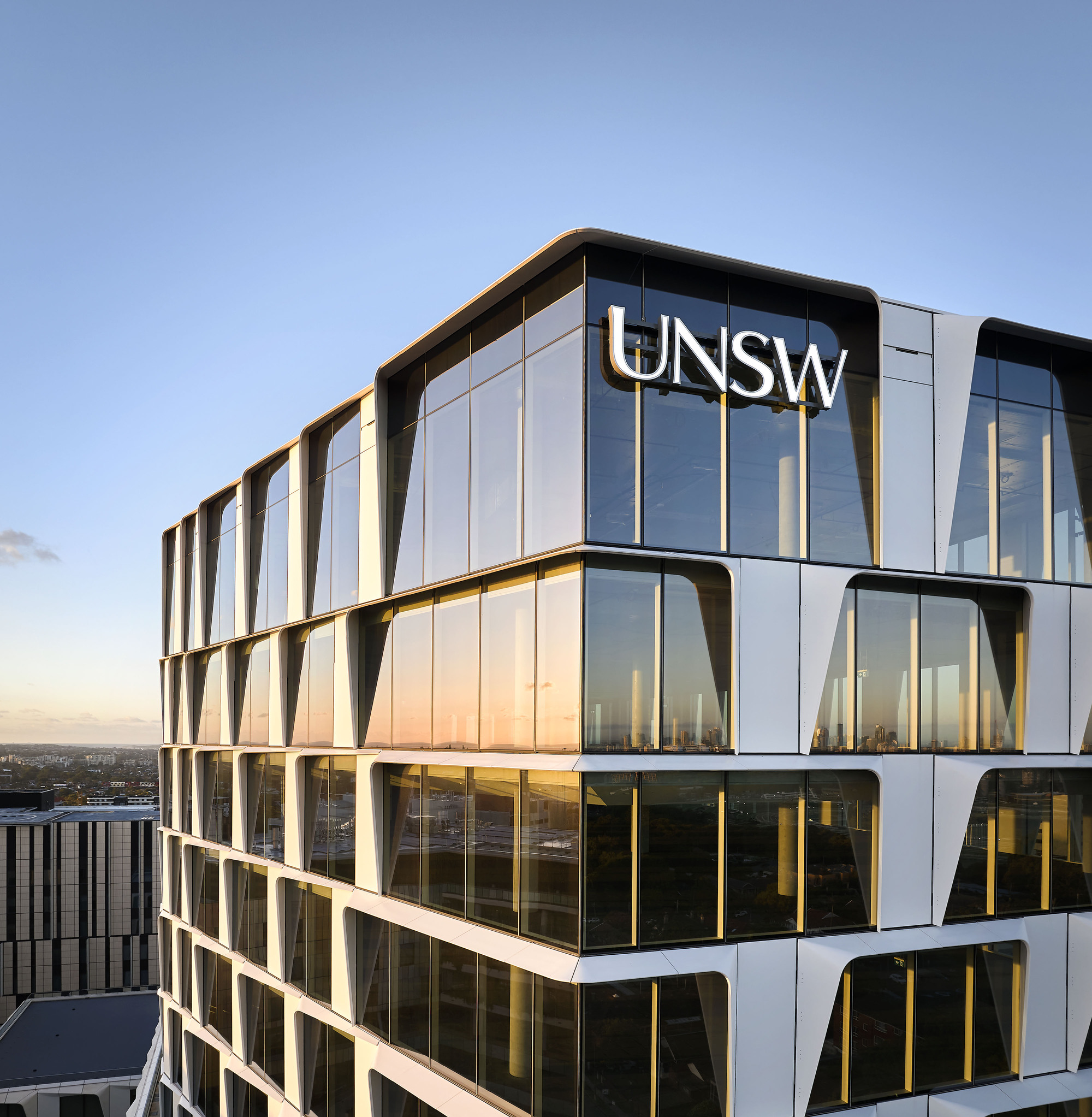 Close-up of the curved glass and metal facade with gold-toned vertical fins at sunset