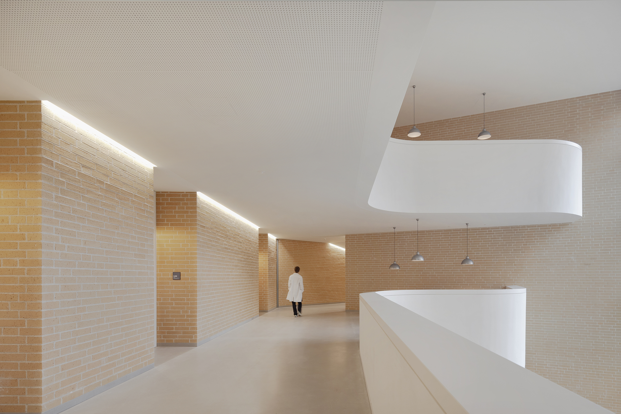 Interior corridor with yellow brick walls and linear cove lighting as a figure walks away