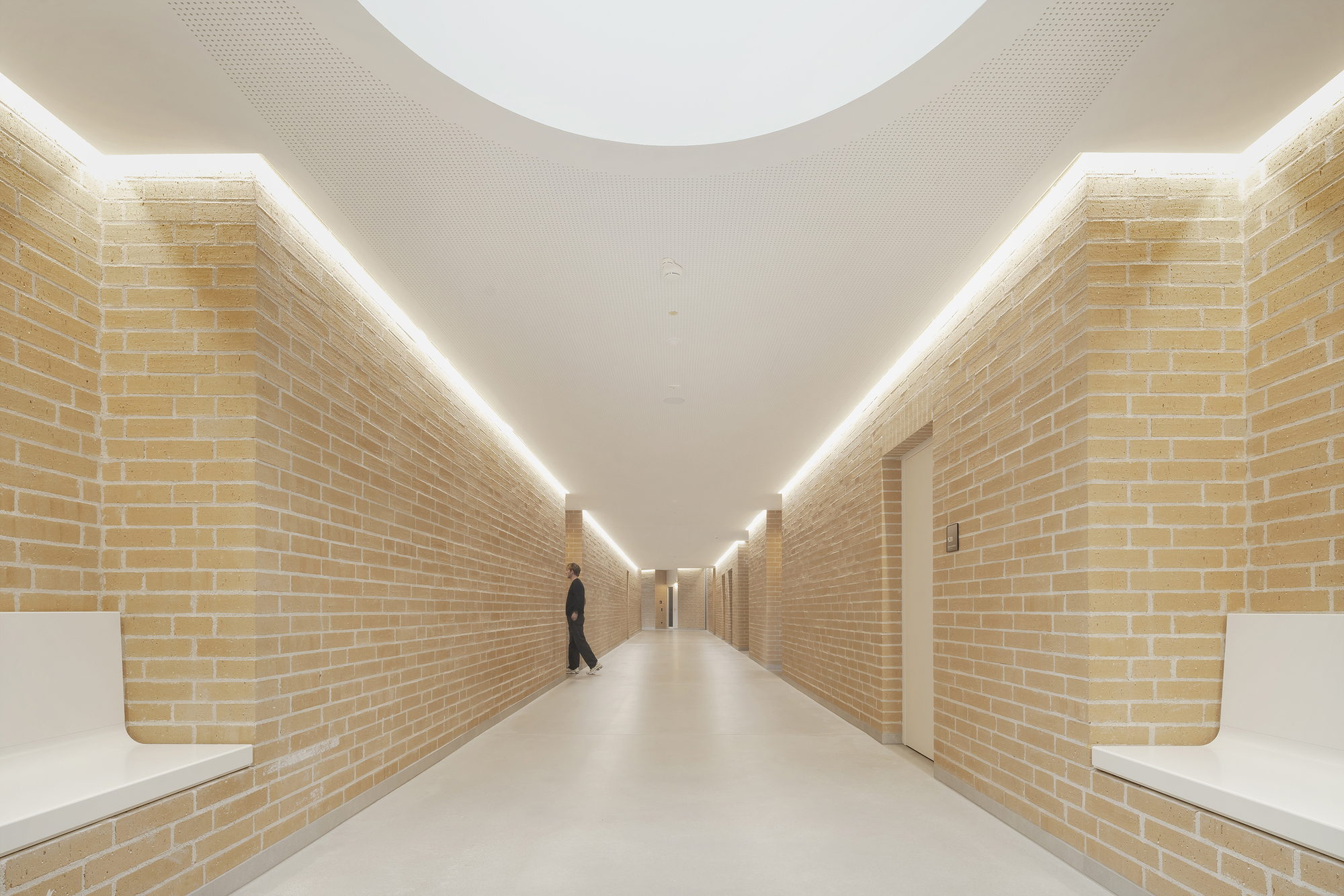 Long corridor with yellow brick walls and continuous linear cove lighting with a walking figure