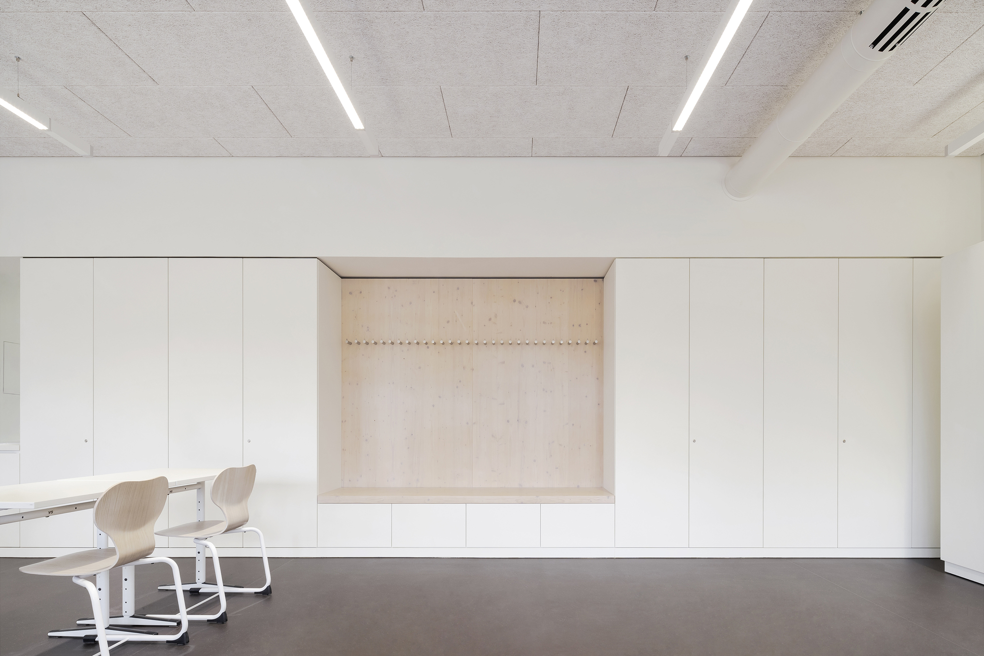 Built-in storage wall with recessed plywood niche and linear LED fixtures in the concrete ceiling