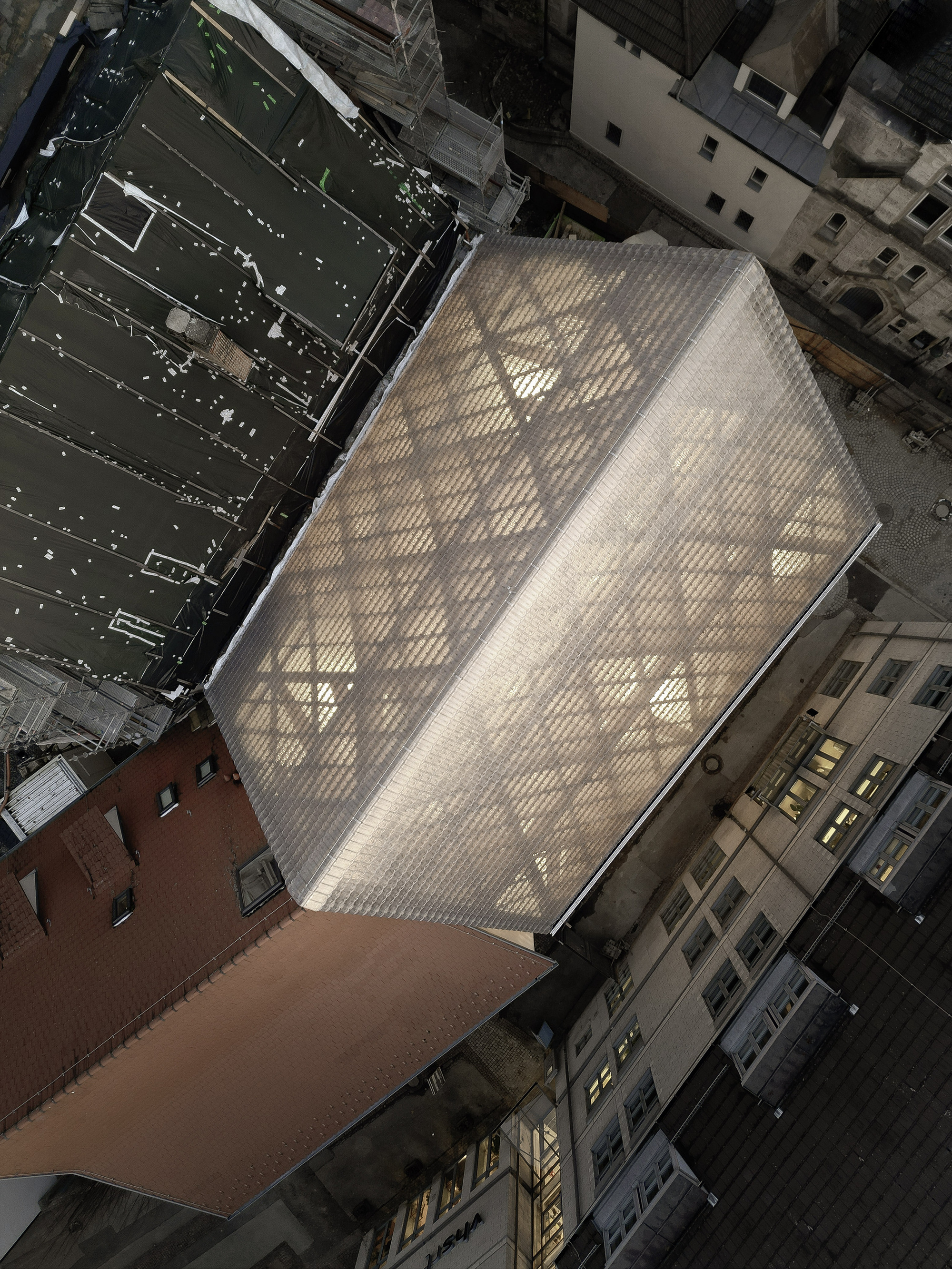 Aerial view of the glass brick volume wedged between neighboring buildings in an urban courtyard